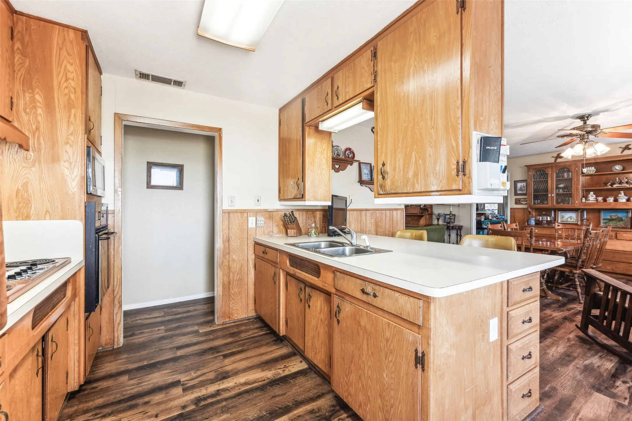Kitchen with dark wood-style floors, light countertops, wainscoting, brown cabinets, and ceiling fan