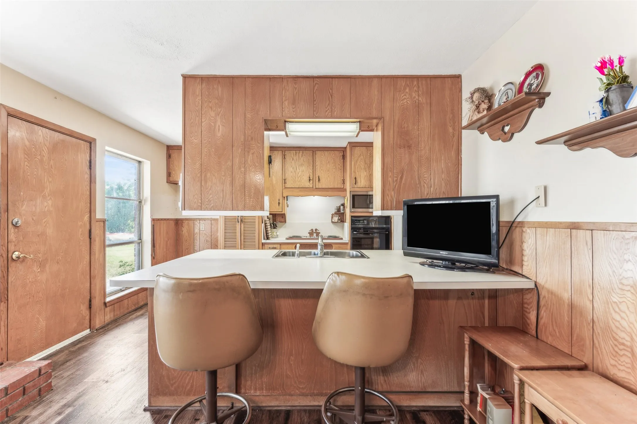Kitchen with light countertops, brown cabinets, a wainscoted wall, wood walls, and dark wood-type flooring