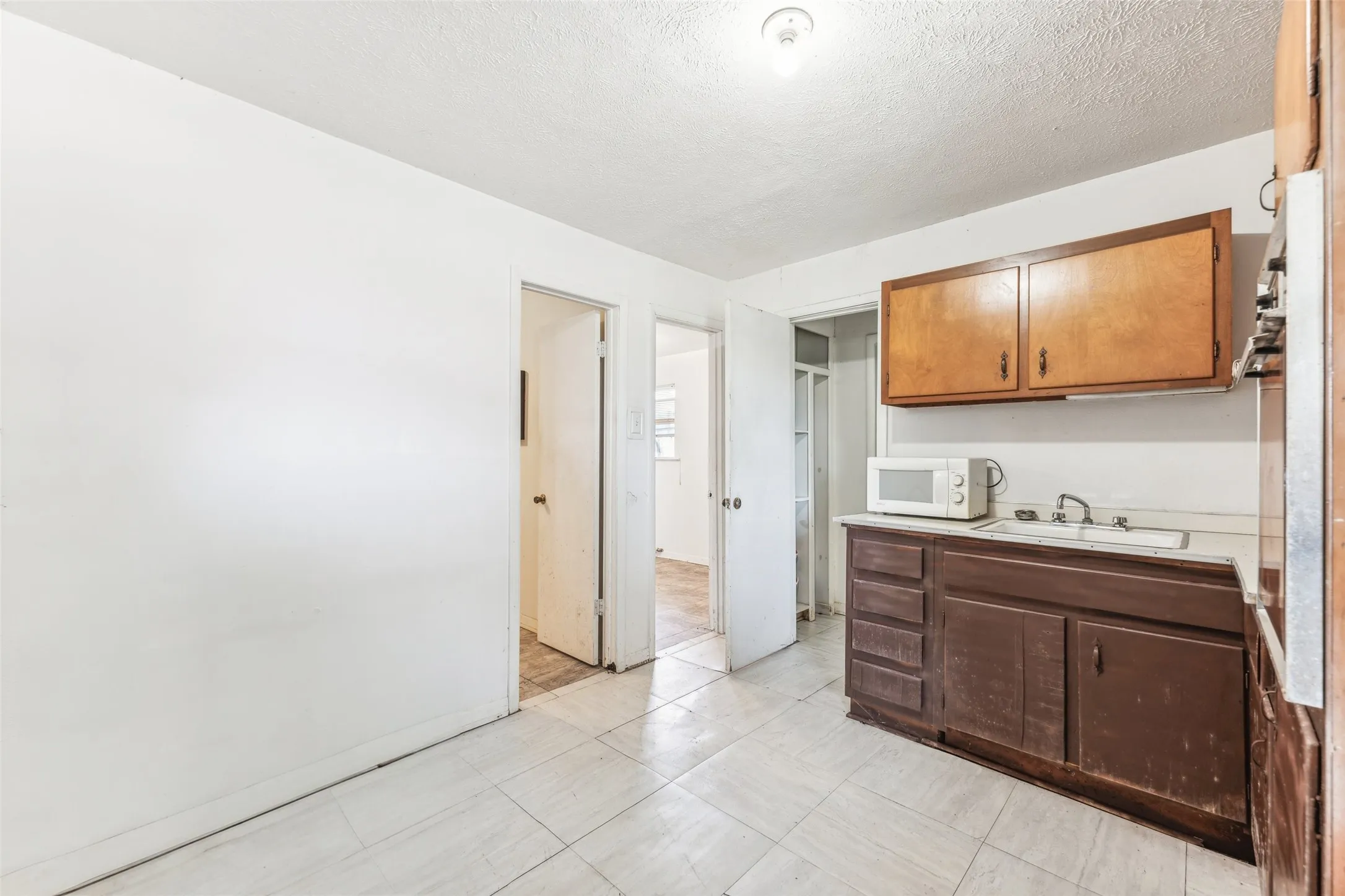 Kitchen featuring light countertops, white microwave, a textured ceiling, oven, and light tile patterned floors