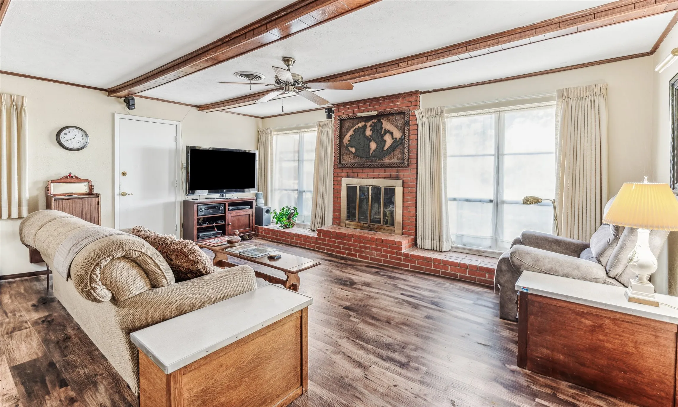 Living area featuring beamed ceiling, dark wood-type flooring, a ceiling fan, and a brick fireplace