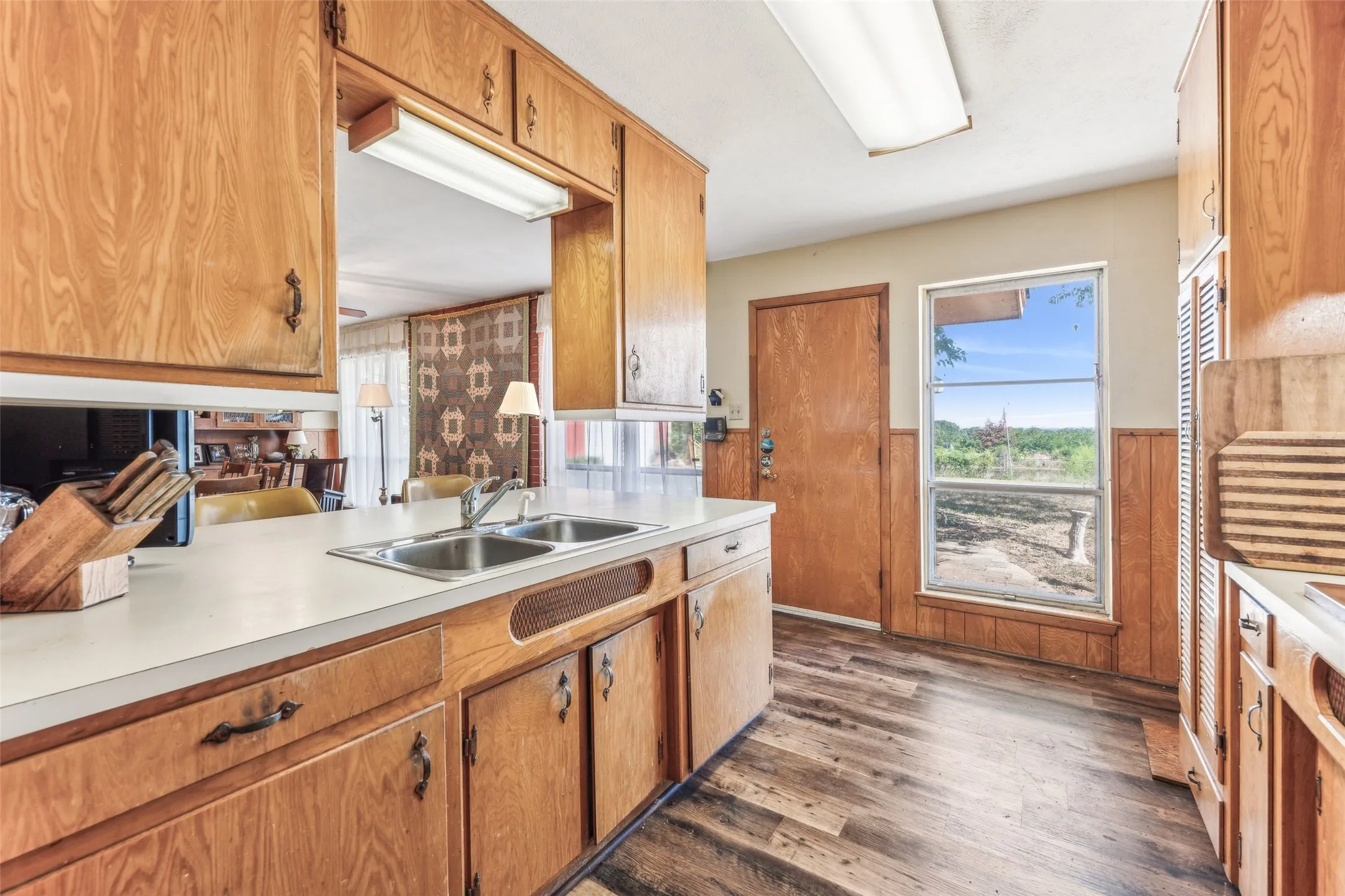 Kitchen with dark wood-style flooring, light countertops, brown cabinetry, wainscoting, and wood walls