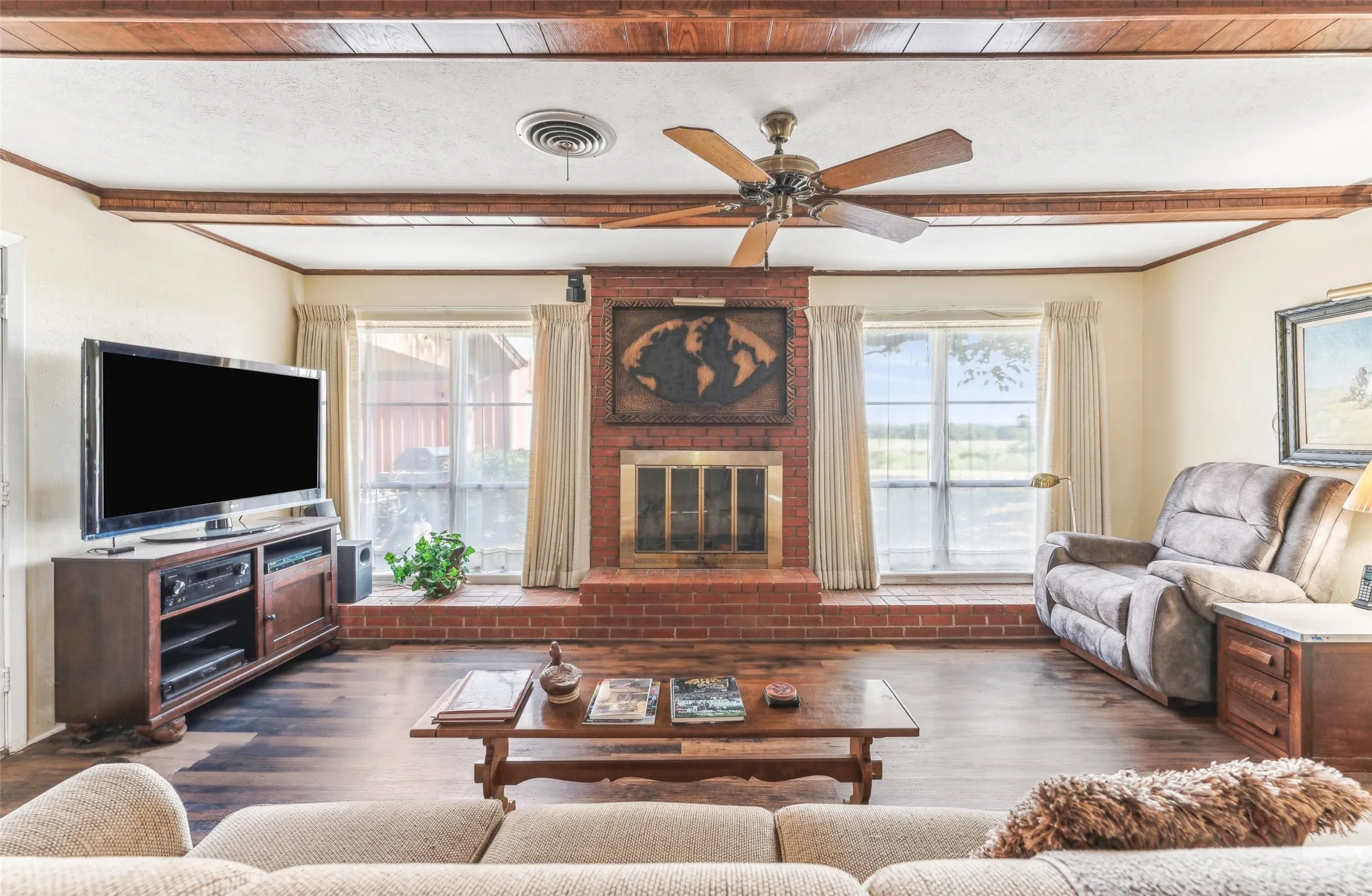 Living area with beamed ceiling, dark wood-style floors, a ceiling fan, a fireplace, and crown molding