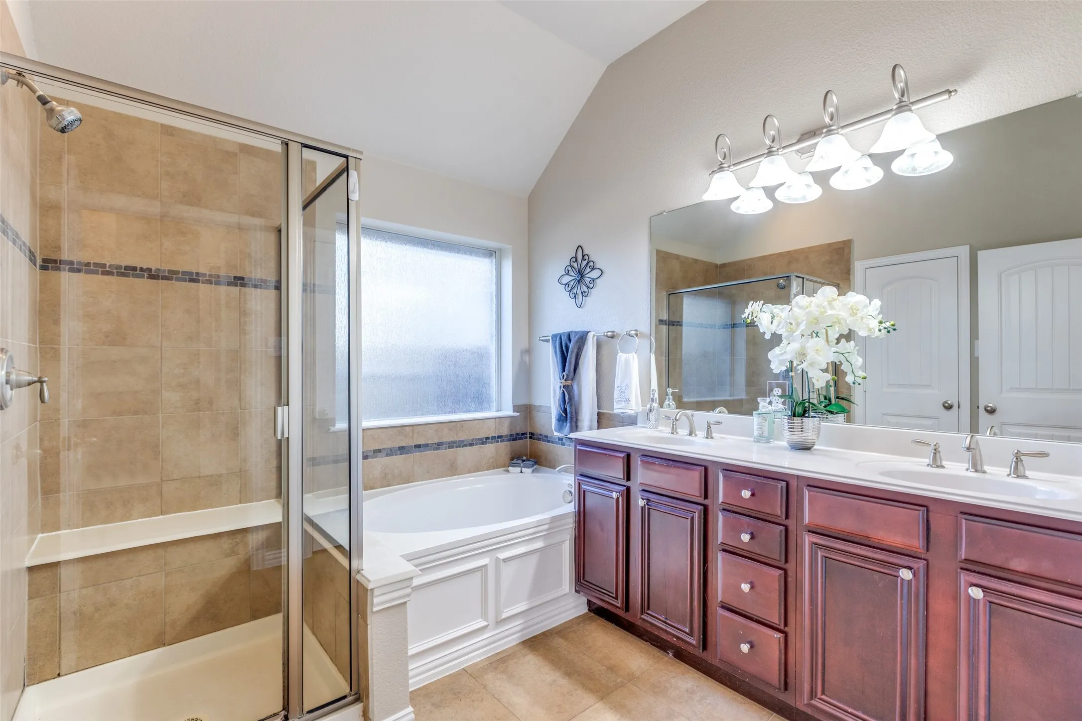 Master bathroom with a garden tub, double vanity, a shower stall, vaulted ceiling, and light tile patterned floors