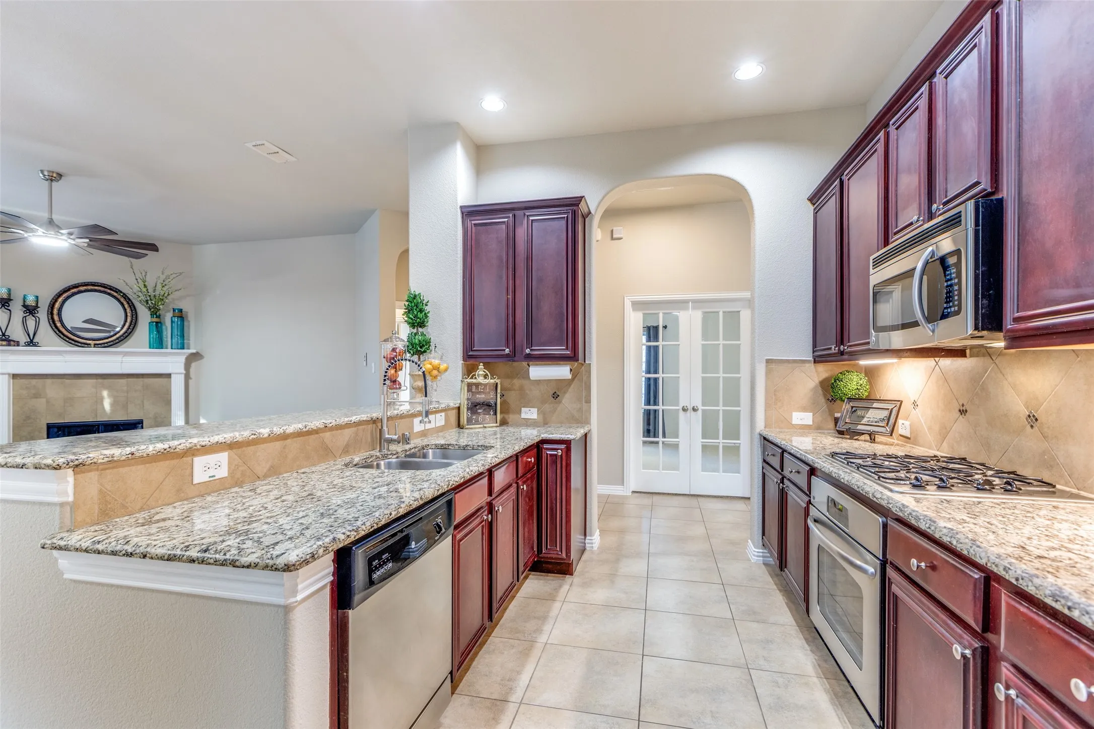 Kitchen with mahogany brown cabinets, a peninsula, tasteful backsplash, light stone countertops, and recessed lighting