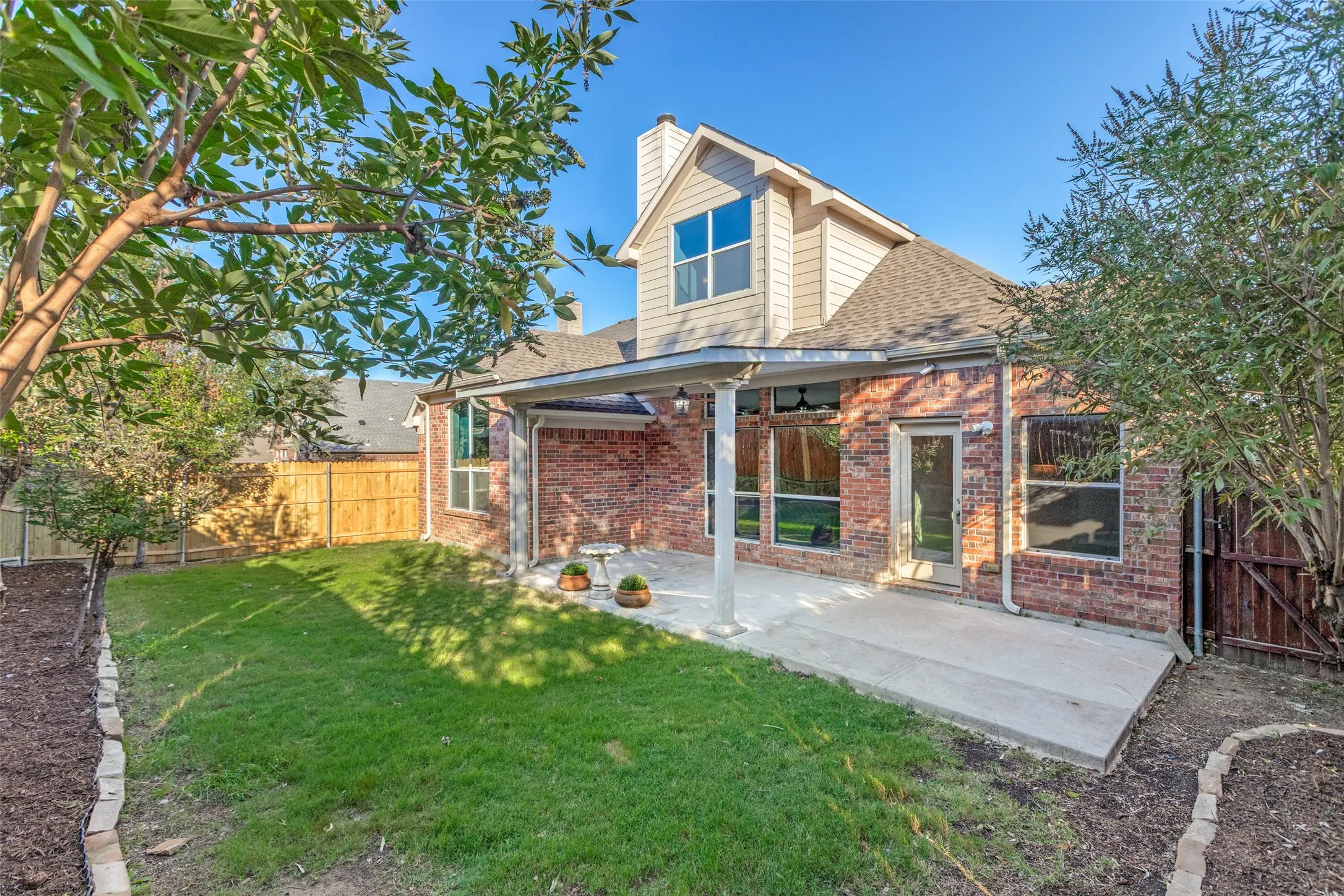 Rear view of property featuring a covered patio area, a fenced backyard, a chimney, a shingled roof, and brick siding