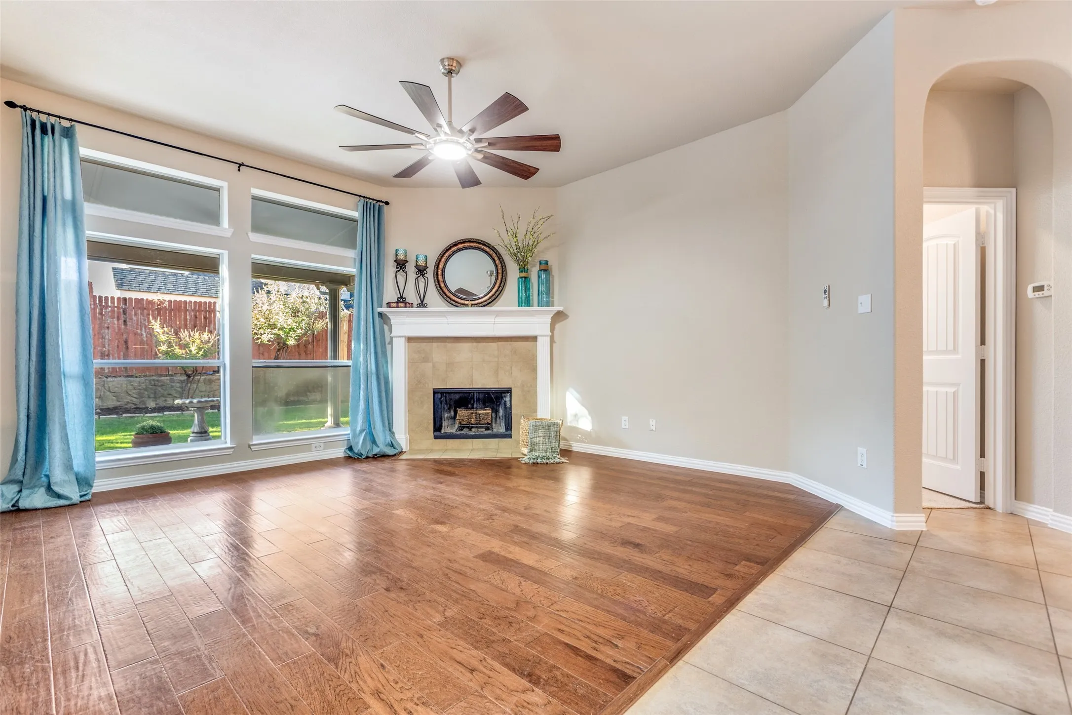Living room with light wood-style flooring, a ceiling fan, a tile fireplace, and arched walkways
