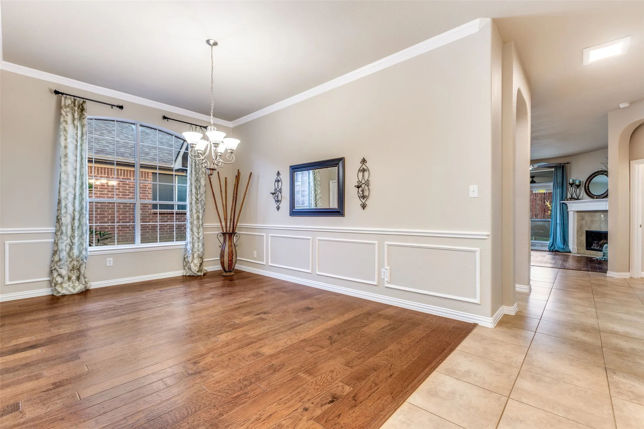 dining area with light wood-type flooring, a tiled fireplace, a chandelier, crown Molding, and arched walkways