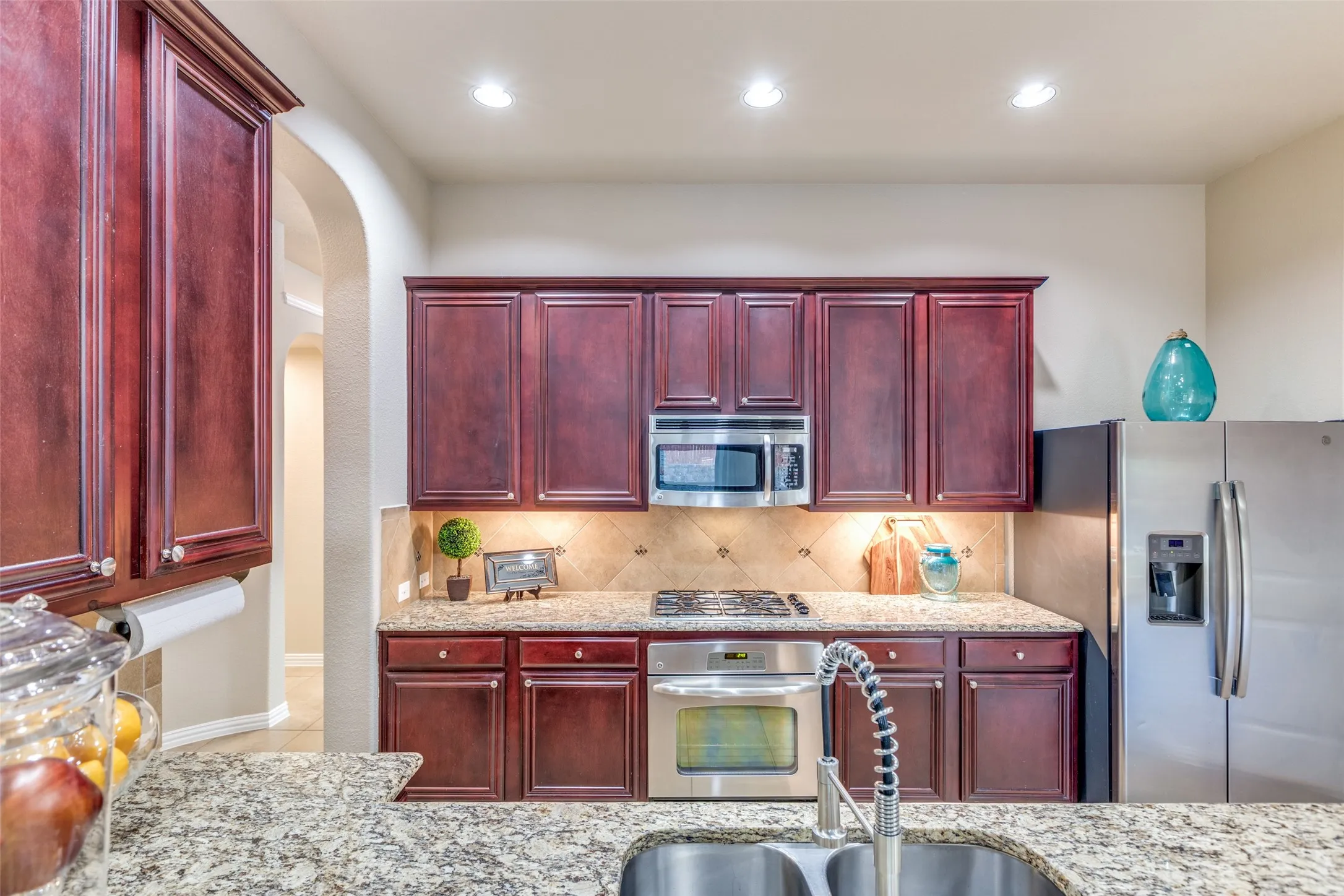 Kitchen with mahogany brown cabinets, stainless steel appliances, light stone countertops, decorative backsplash, and recessed lighting