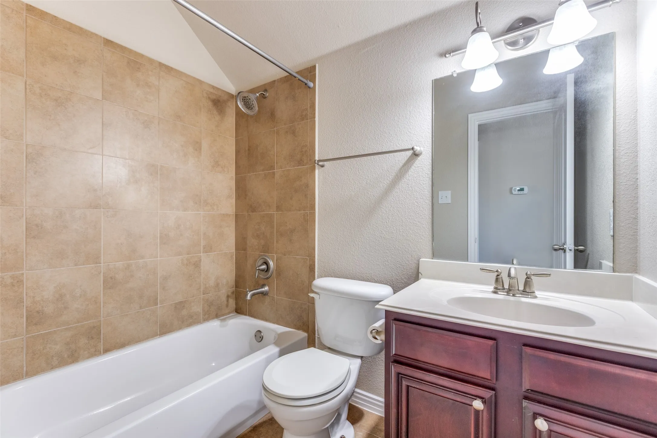 Bathroom with a textured wall, vanity, and shower / bath combination