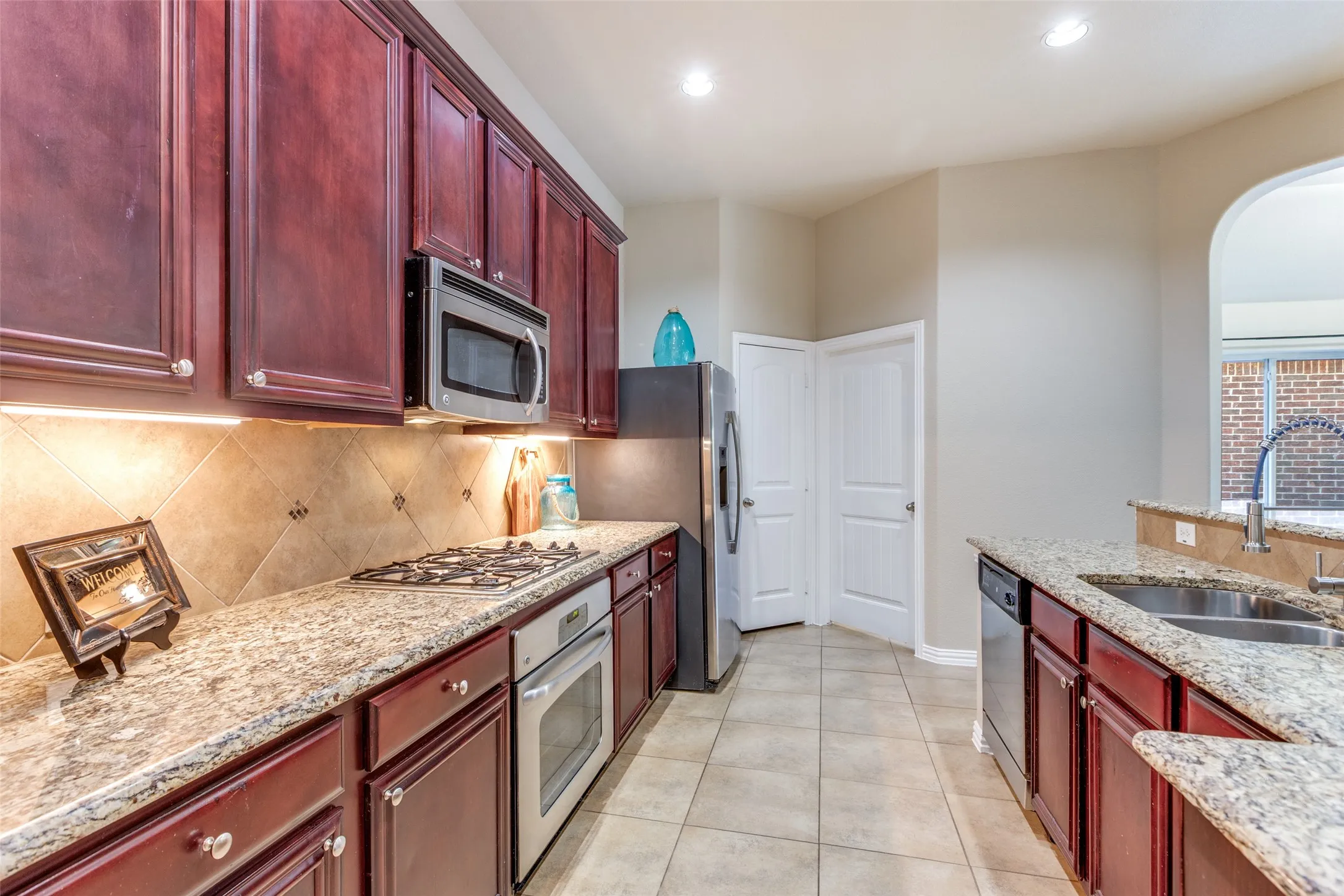 Kitchen featuring reddish brown cabinets, light stone counters, backsplash, stainless steel appliances, and recessed lighting