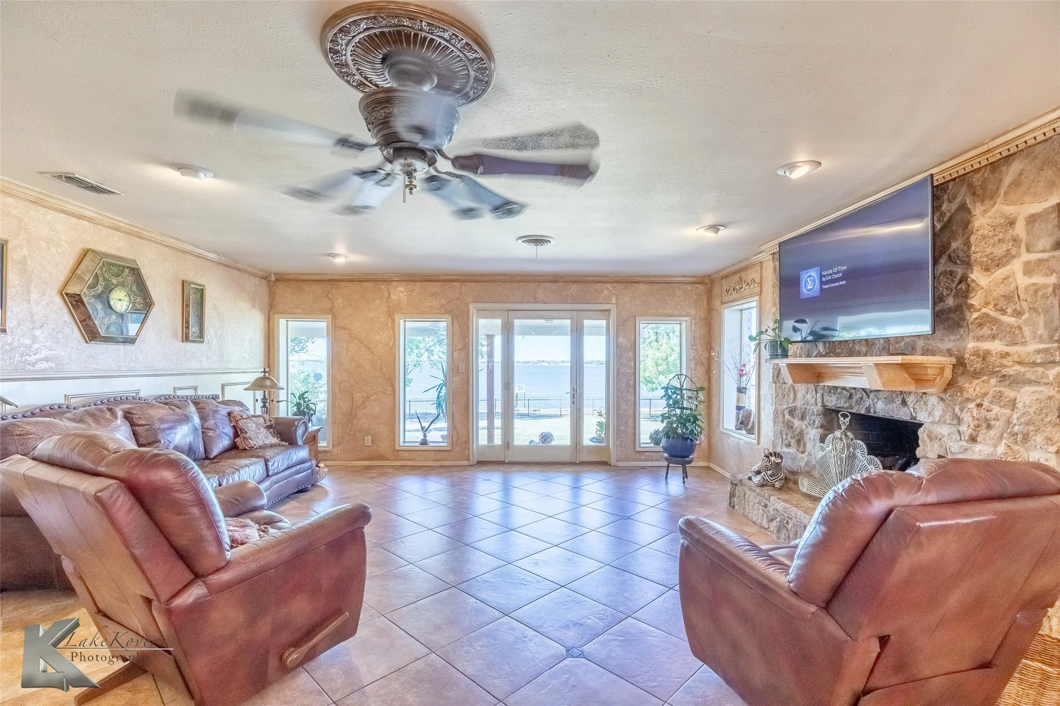 Tiled living room featuring a stone fireplace, crown molding, a ceiling fan, and a textured ceiling