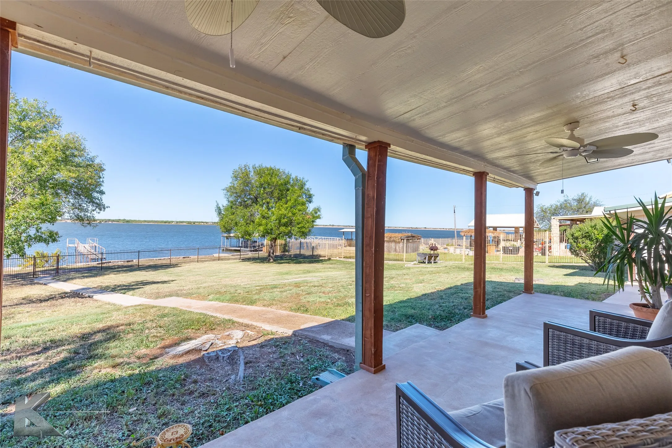 Fenced backyard with ceiling fans and a water view