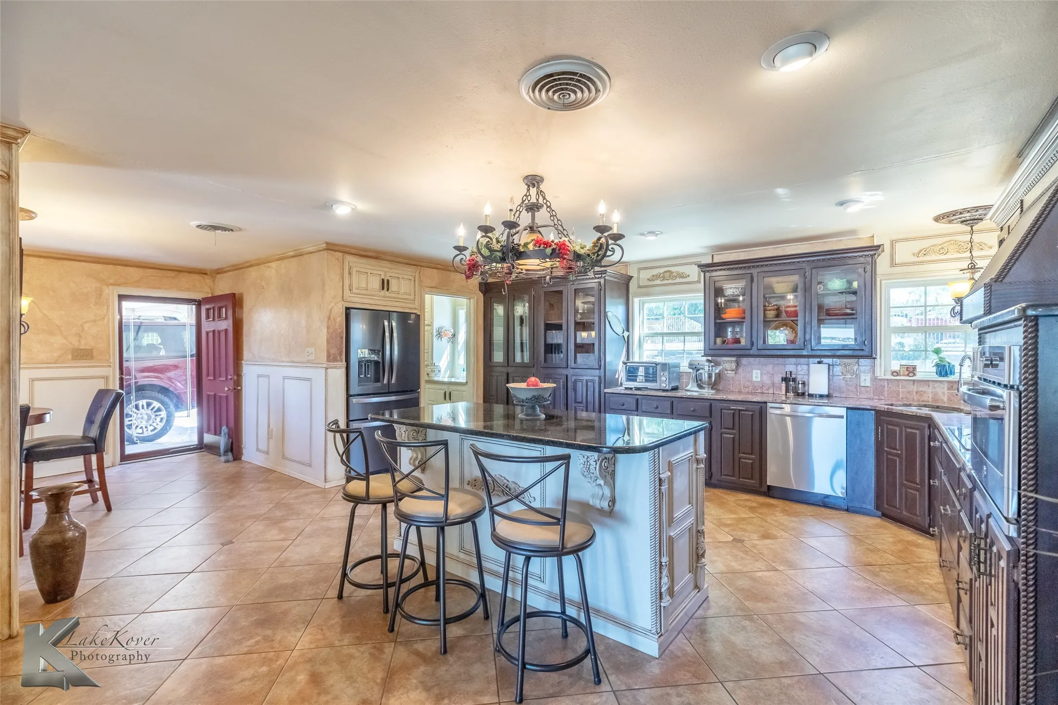 Kitchen featuring hanging light fixtures, stainless steel appliances, a kitchen bar, light tile patterned flooring, and dark stone countertops