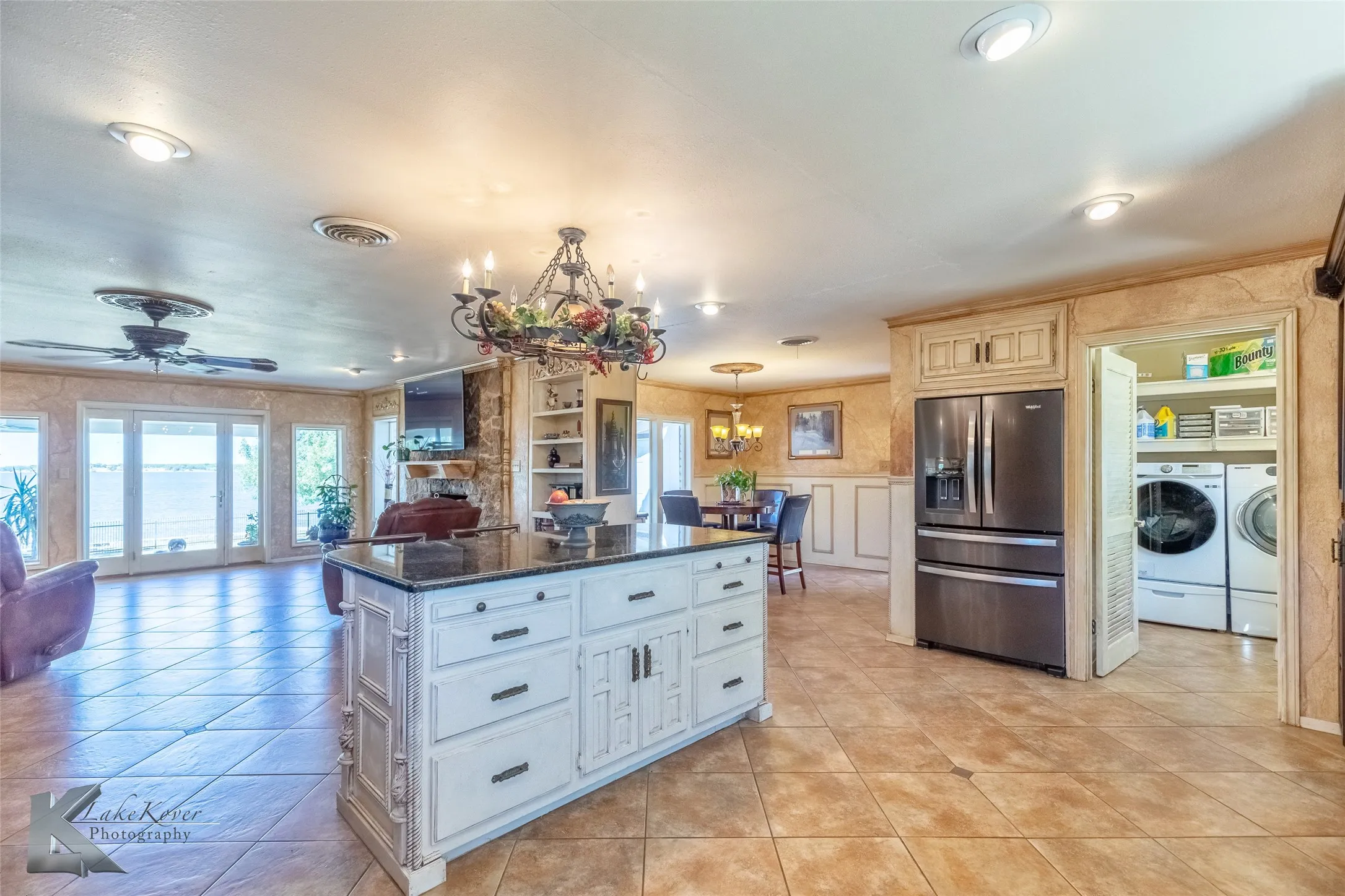 Kitchen featuring decorative light fixtures, stainless steel refrigerator with ice dispenser, open floor plan, dark stone counters, and a center island