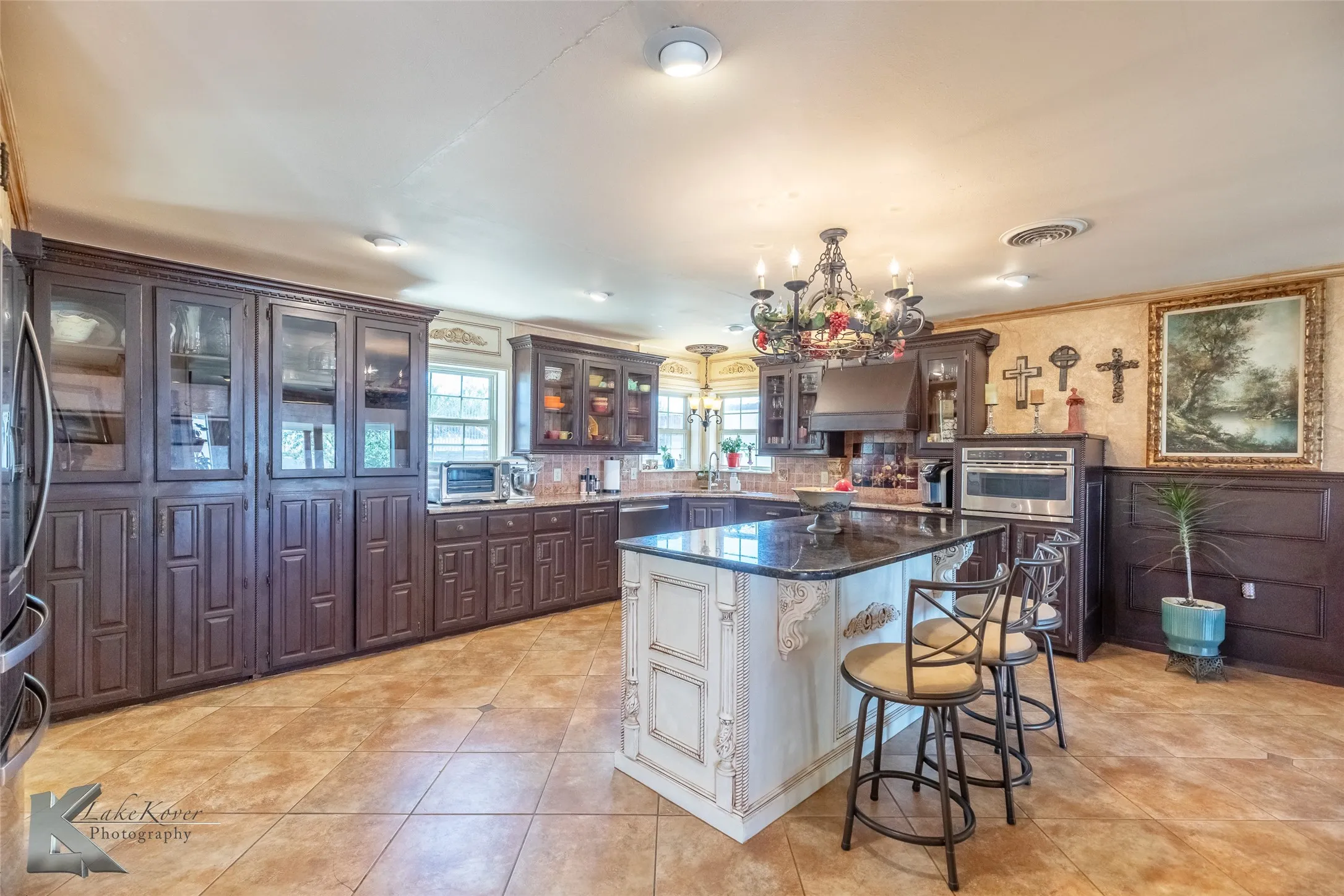 Kitchen with white cabinets, a kitchen bar, a chandelier, glass insert cabinets, and dark brown cabinetry