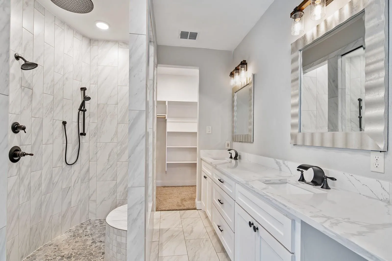 Bathroom featuring double vanity, a spacious closet, walk in shower, light marble finish flooring, and recessed lighting