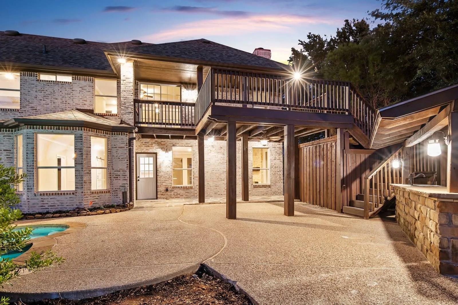 Back of house at dusk featuring a patio area, a balcony, stairway, and brick siding