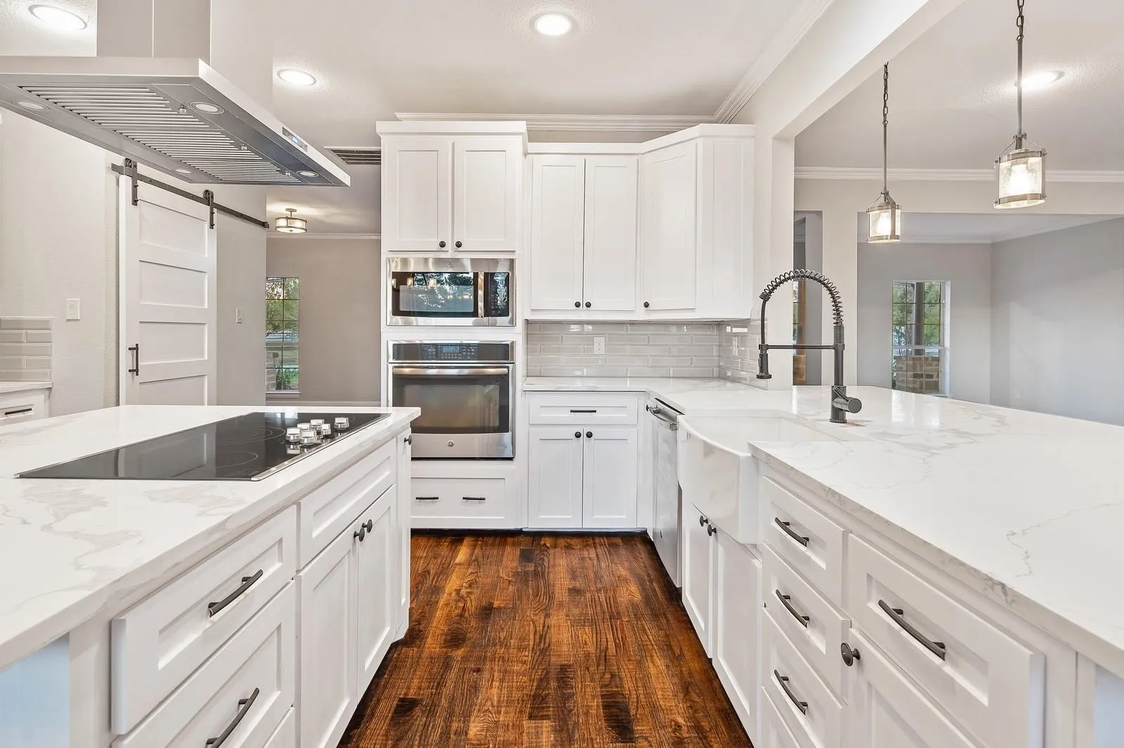 Kitchen with exhaust hood, light stone countertops, white cabinets, appliances with stainless steel finishes, and healthy amount of natural light
