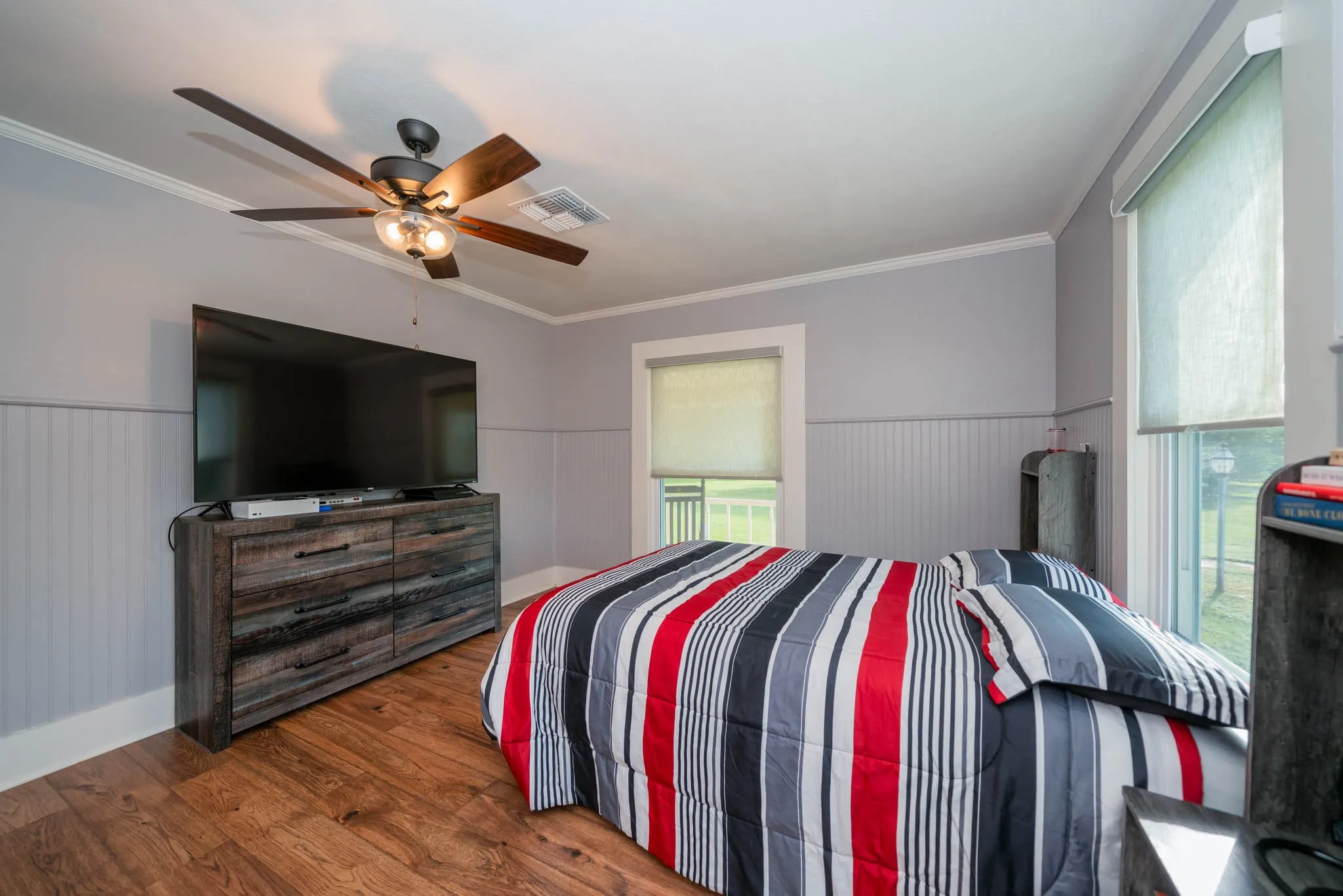 Bedroom featuring wainscoting, crown molding, wood finished floors, and a ceiling fan