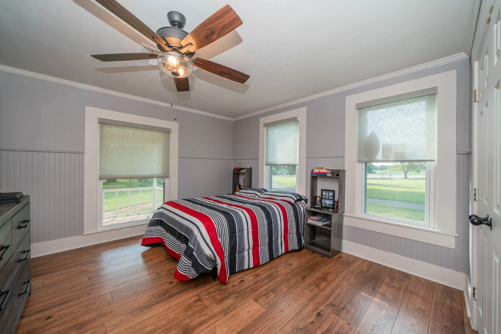 Bedroom with crown molding, wainscoting, dark wood-style flooring, ceiling fan, and wooden walls