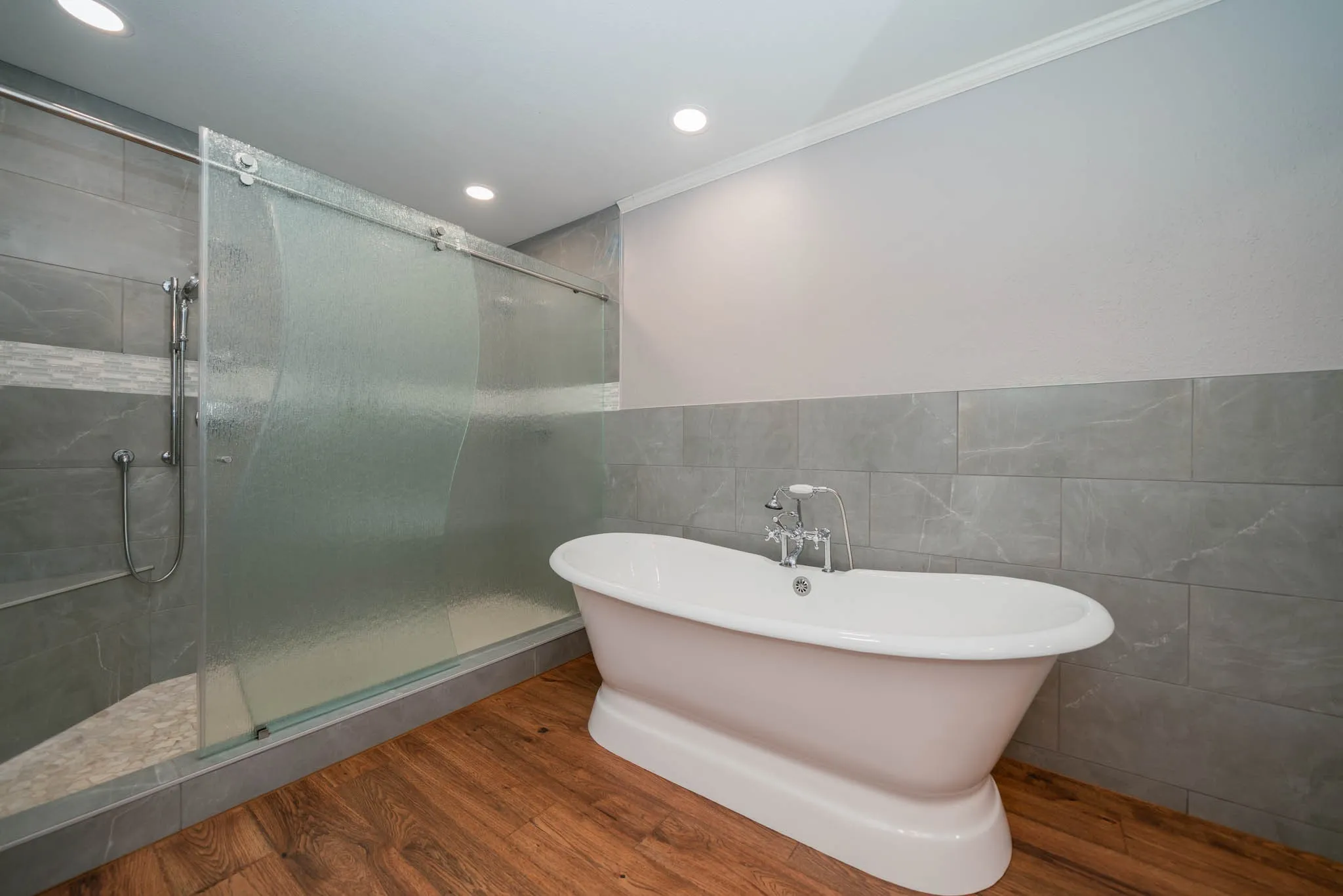 Bathroom featuring wood finished floors, a soaking tub, tile walls, a shower stall, and crown molding