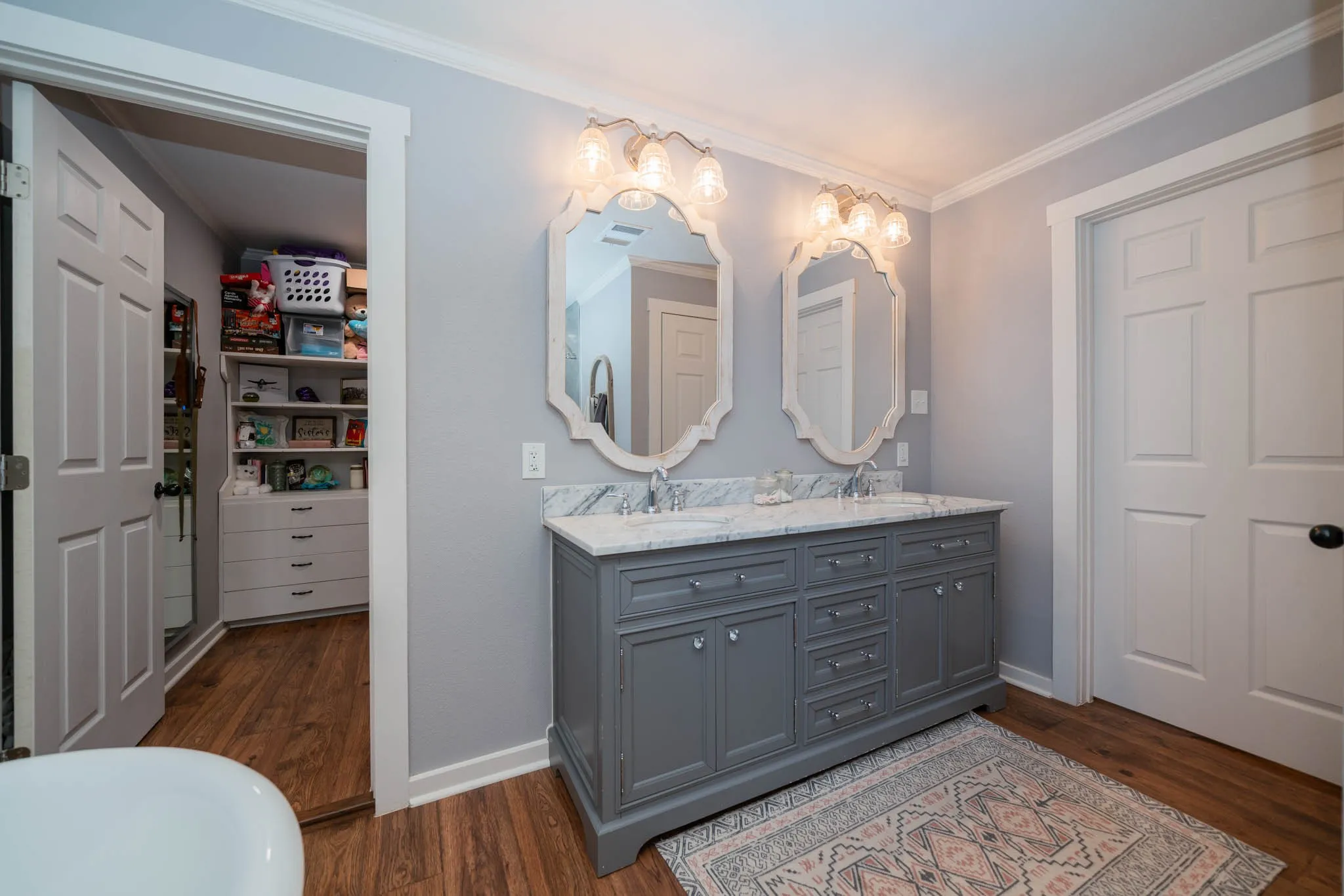 Full bath with dark wood-style flooring, crown molding, and double vanity