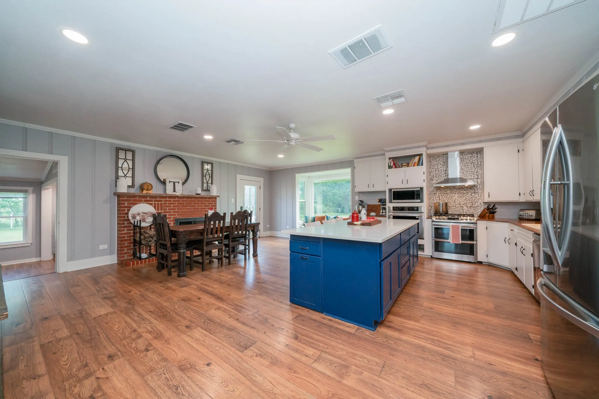 Kitchen featuring blue cabinets, stainless steel appliances, white cabinetry, wall chimney range hood, and a kitchen island