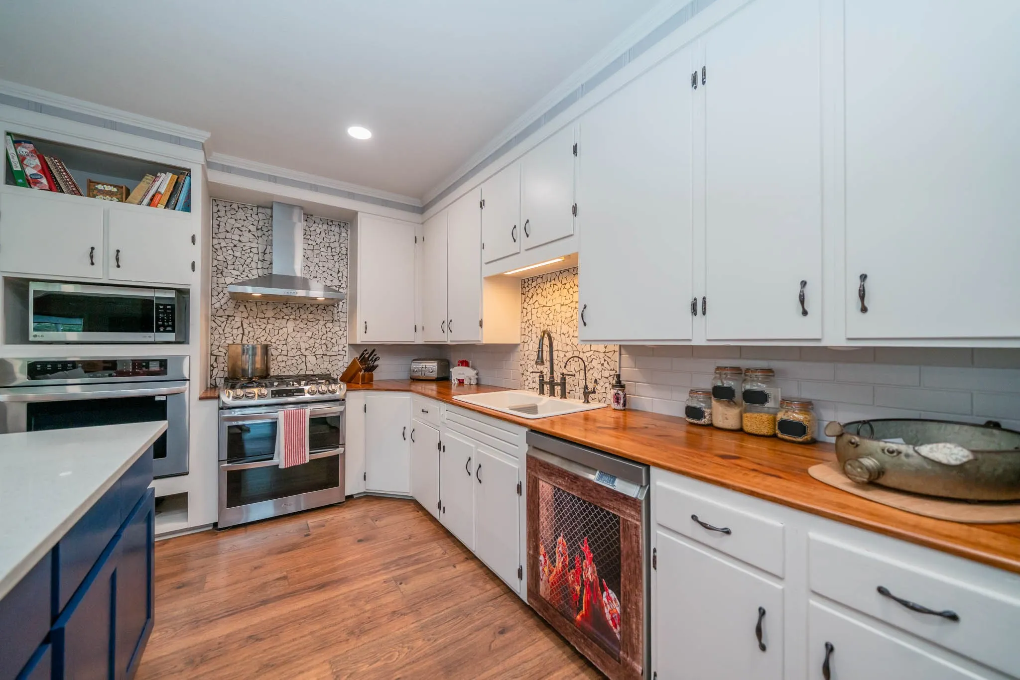Kitchen featuring appliances with stainless steel finishes, light wood-style floors, white cabinets, wall chimney exhaust hood, and backsplash