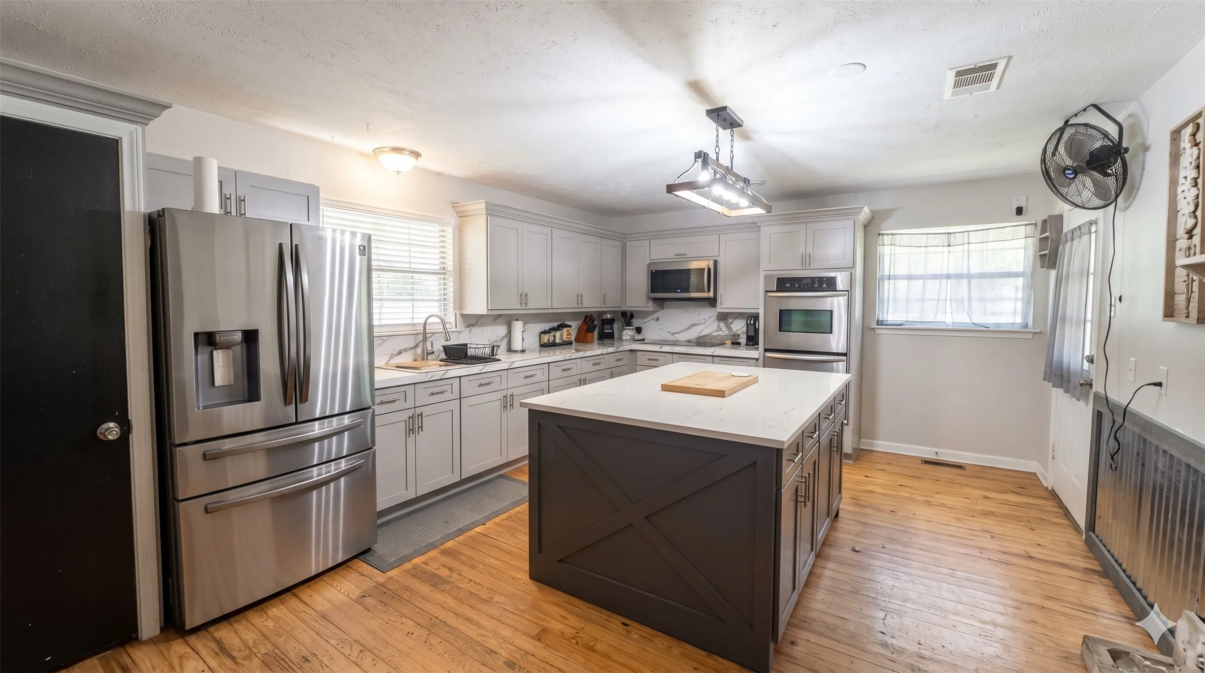 Kitchen with stainless steel fridge with ice dispenser, light wood-style flooring, a textured ceiling, light stone countertops, and decorative light fixtures