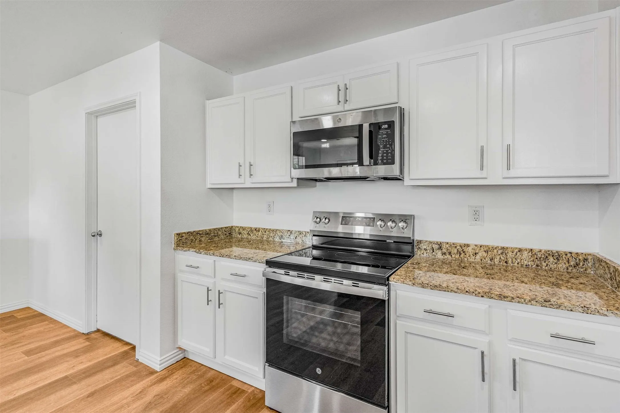 Kitchen featuring appliances with stainless steel finishes, white cabinetry, light wood-style floors, and light stone countertops
