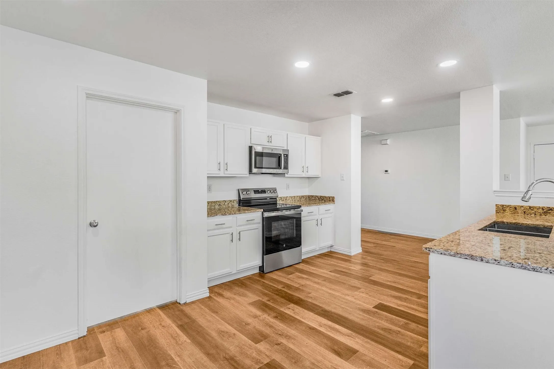 Kitchen with stainless steel appliances, light wood-style flooring, recessed lighting, light stone countertops, and white cabinetry