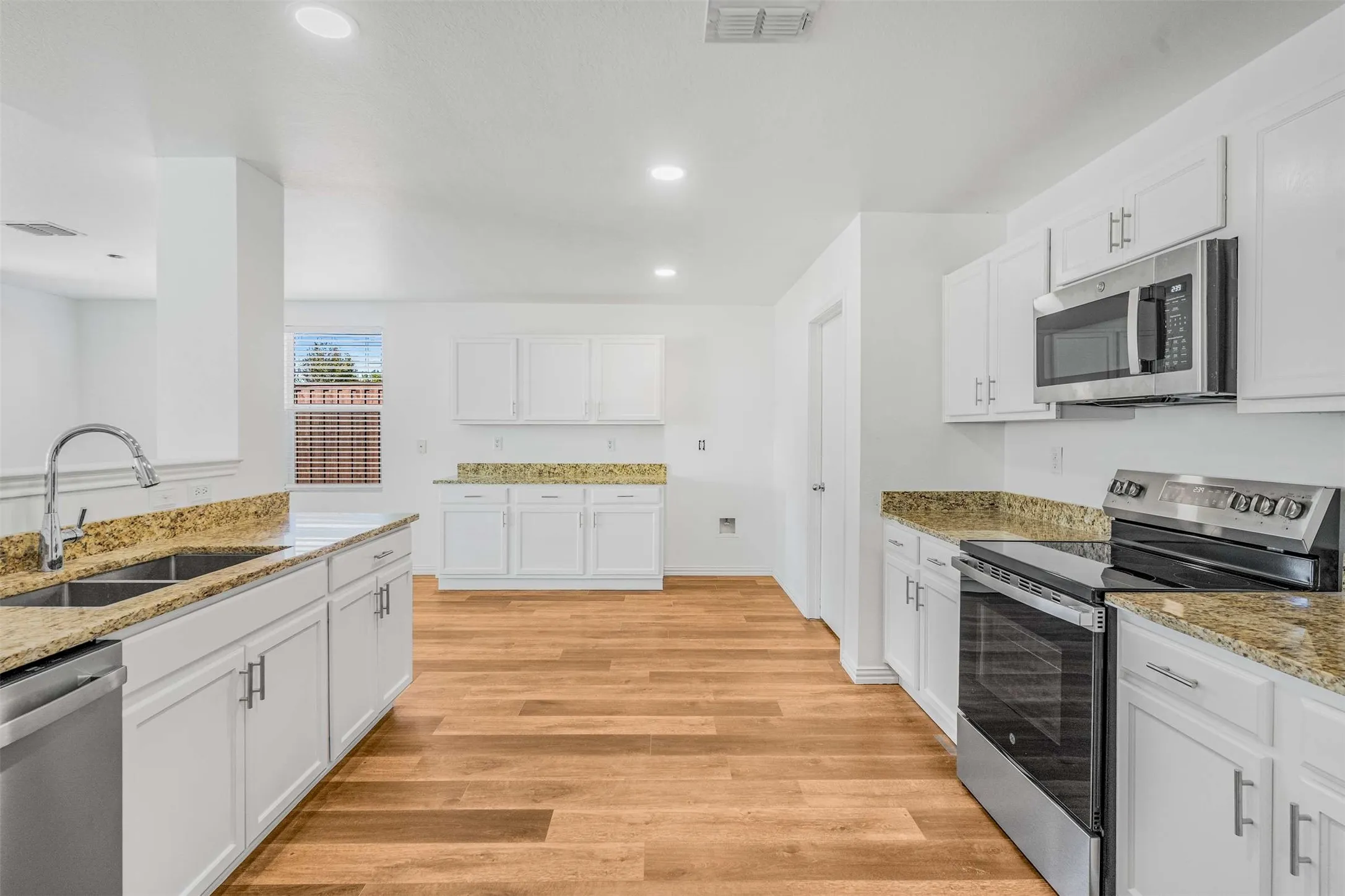 Kitchen featuring stainless steel appliances, white cabinetry, light stone counters, light wood-type flooring, and recessed lighting