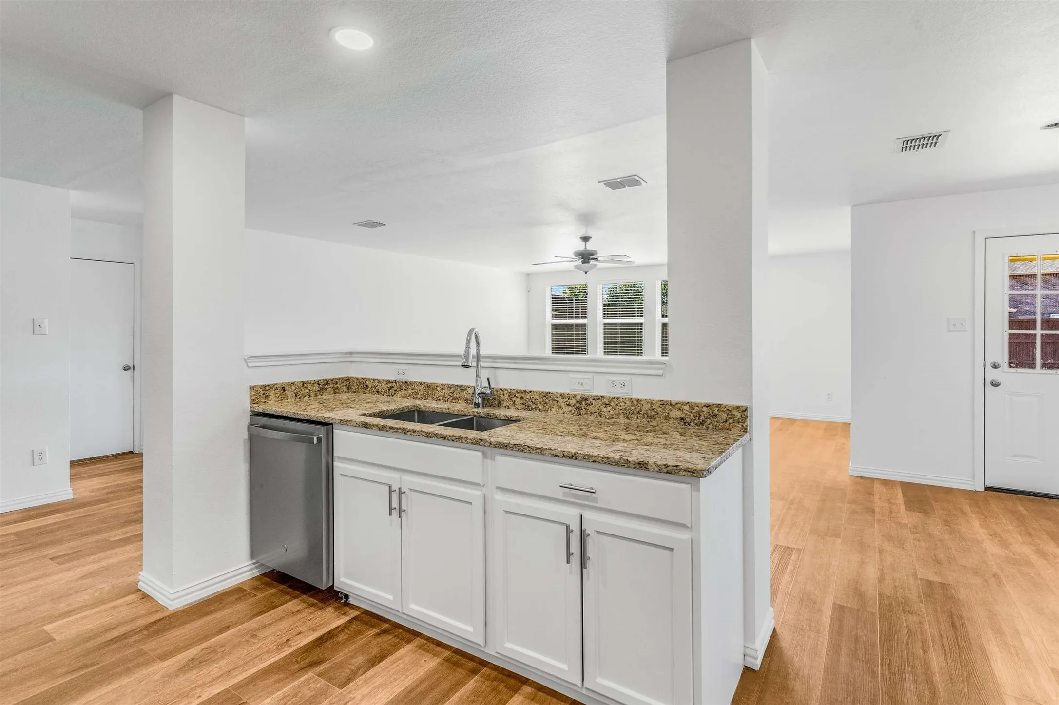 Kitchen featuring white cabinets, light stone counters, light wood-style flooring, and stainless steel dishwasher