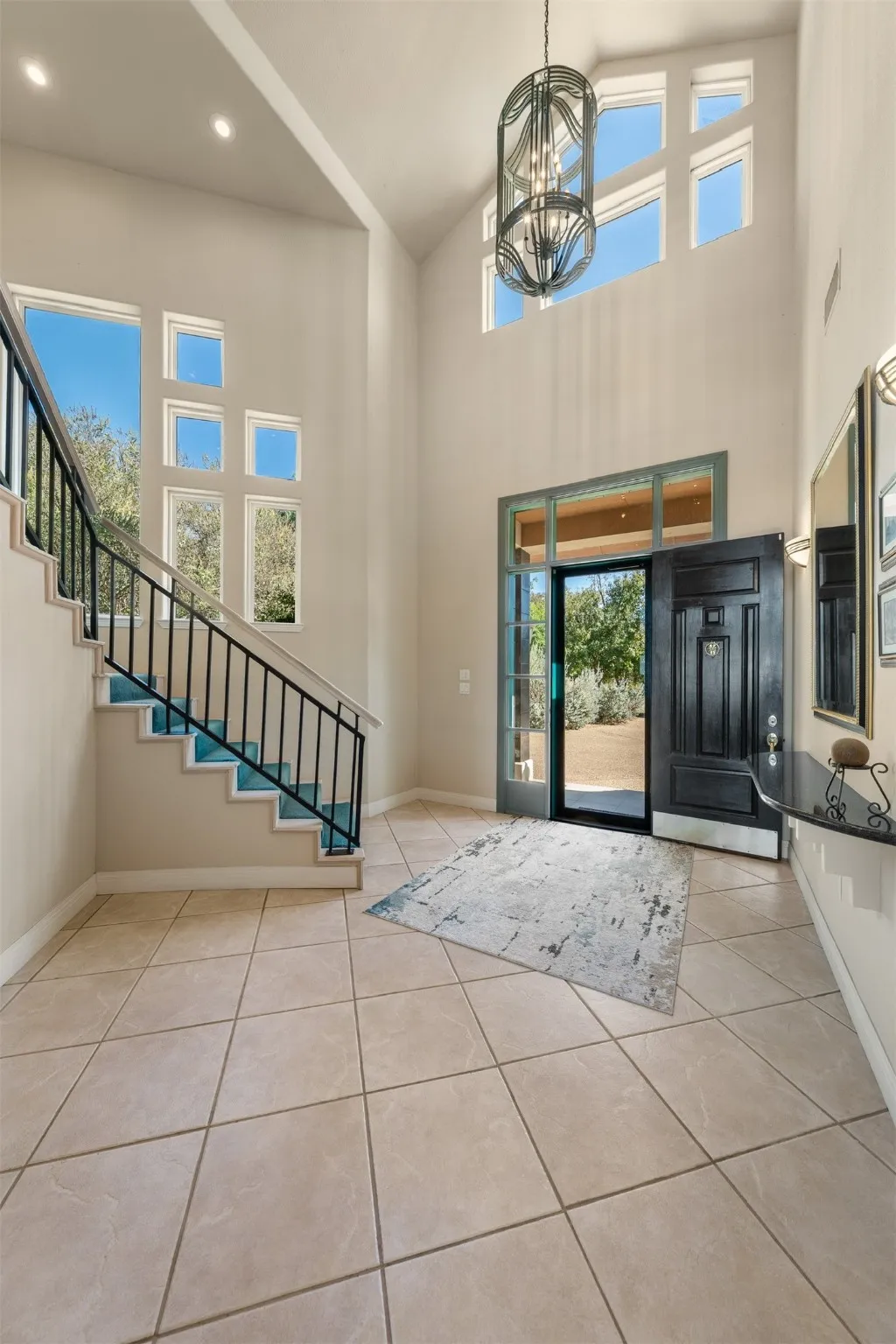 Entrance foyer with stairs, light tile patterned floors, high vaulted ceiling, and a chandelier