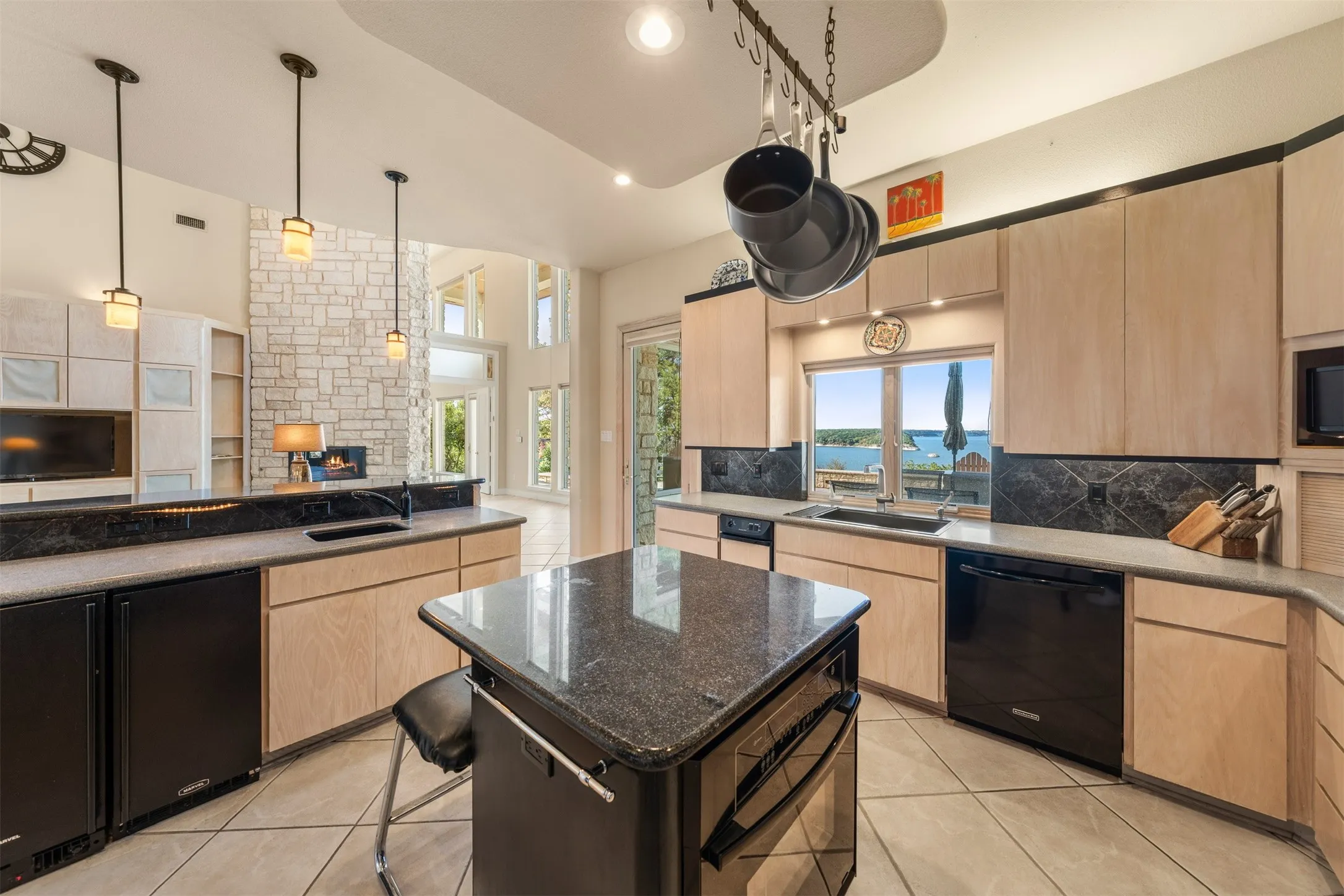 Kitchen featuring light brown cabinets, black appliances, backsplash, pendant lighting, and dark stone countertops