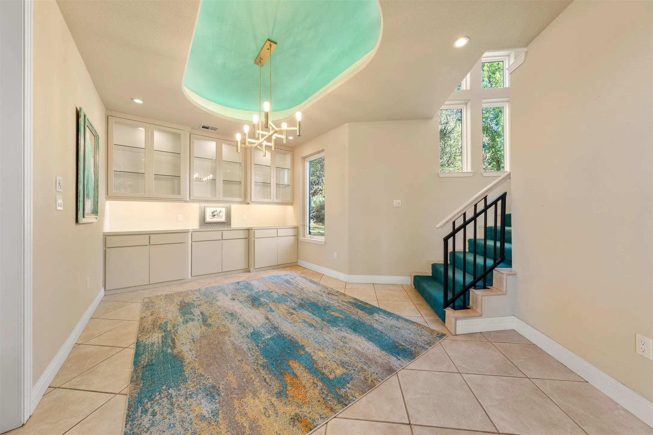 Unfurnished dining area featuring a tray ceiling, stairs, light tile patterned floors, recessed lighting, and a chandelier