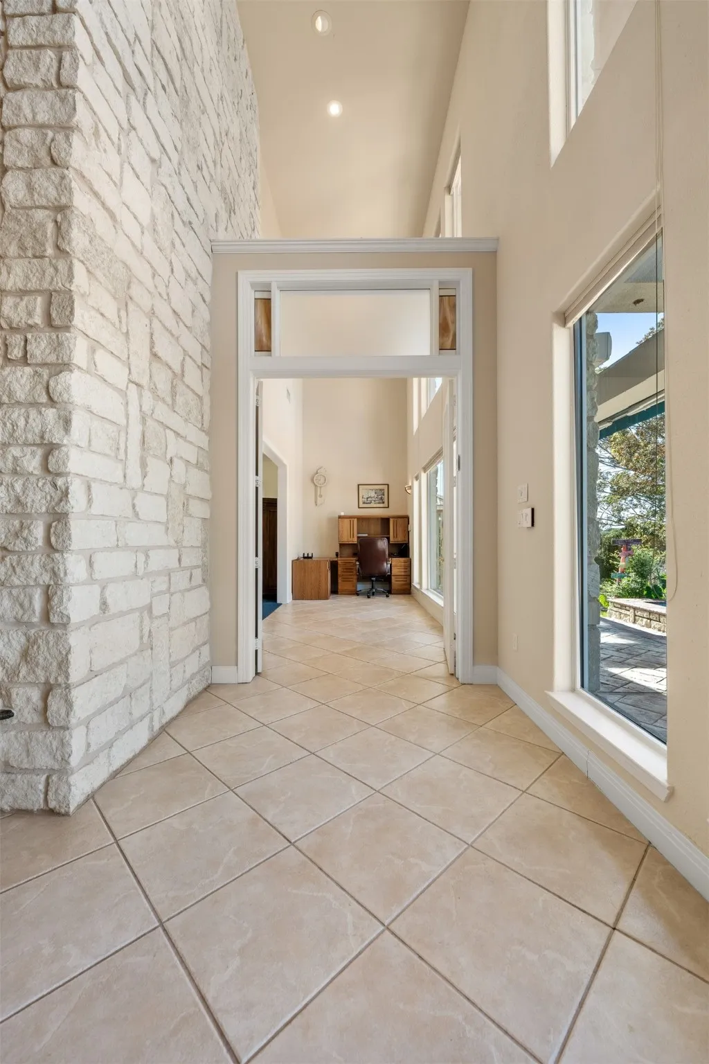 Hallway featuring a high ceiling, light tile patterned floors, recessed lighting, and a desk