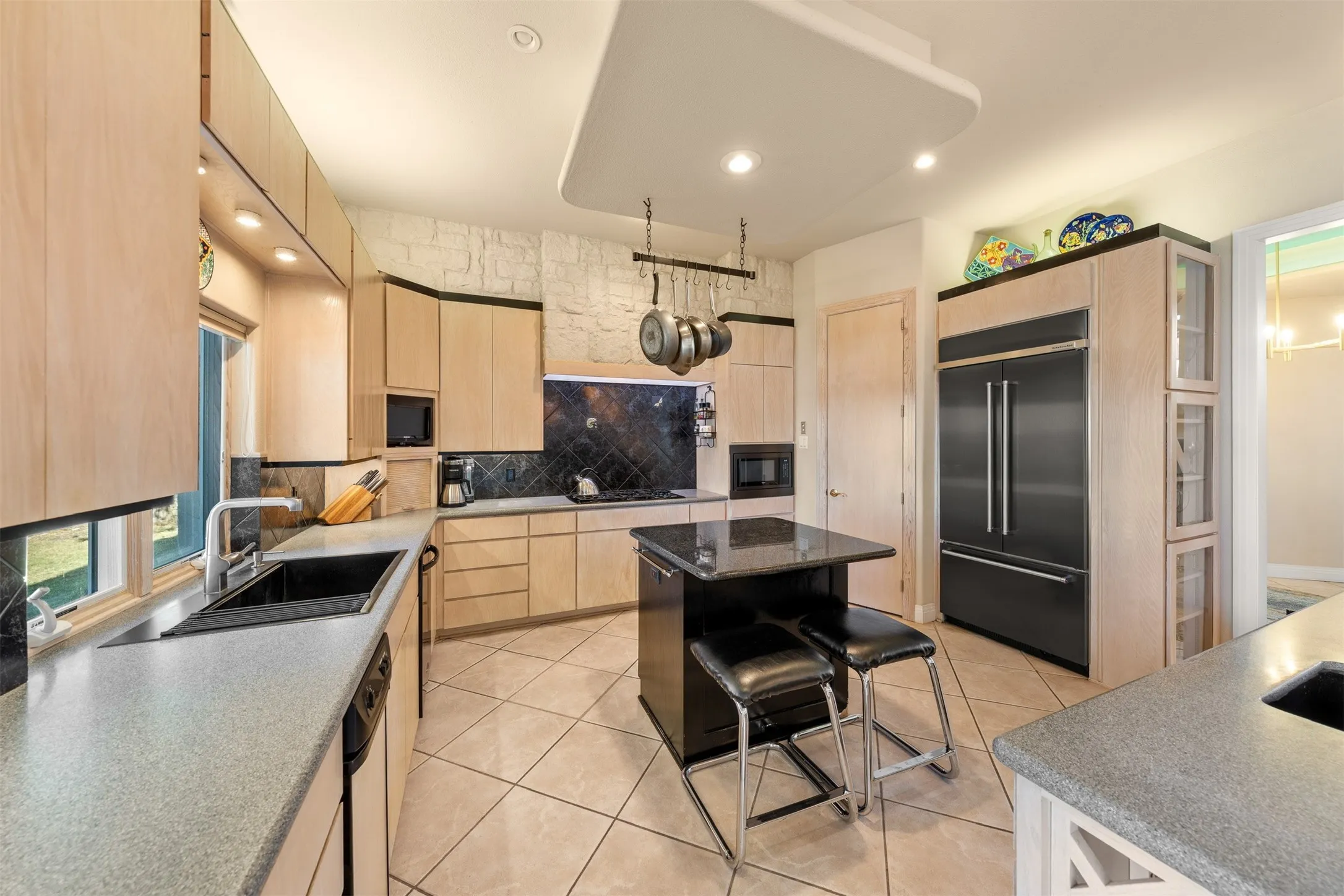 Kitchen featuring light brown cabinets, decorative backsplash, built in appliances, light tile patterned flooring, and a kitchen bar