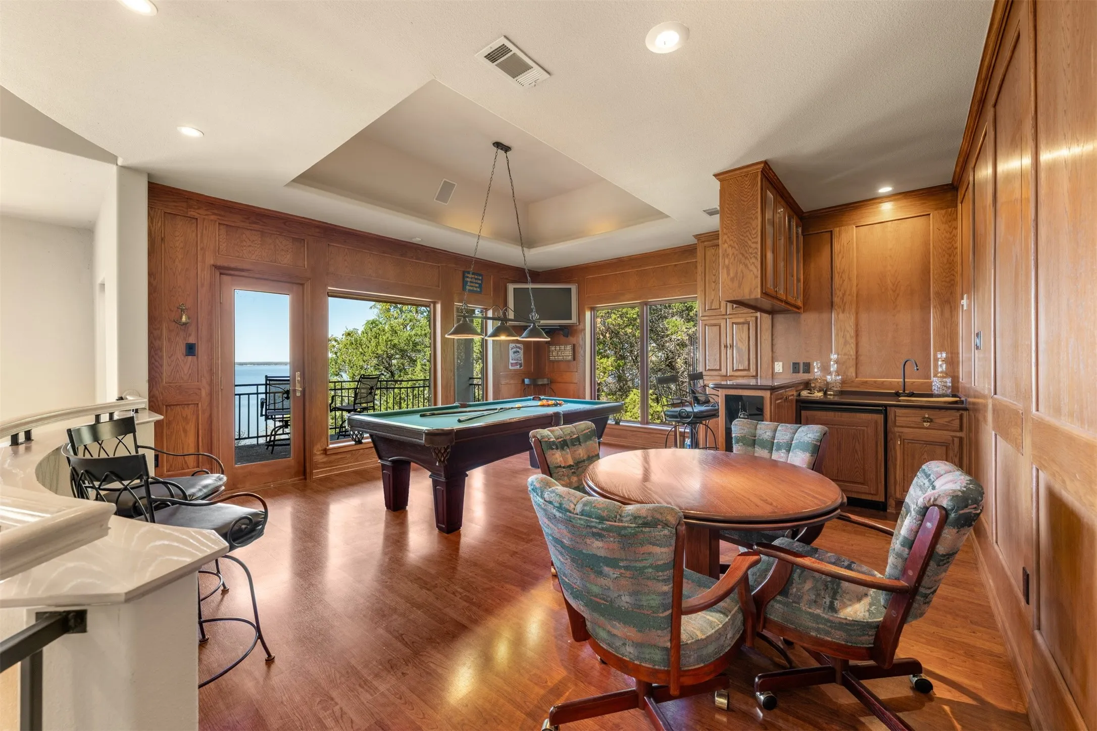 Game room featuring a raised ceiling, pool table, light wood-style floors, wood walls, and recessed lighting
