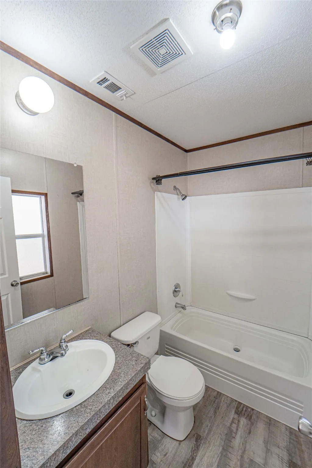Bathroom with ornamental molding, light wood-type flooring, washtub / shower combination, vanity, and a textured ceiling