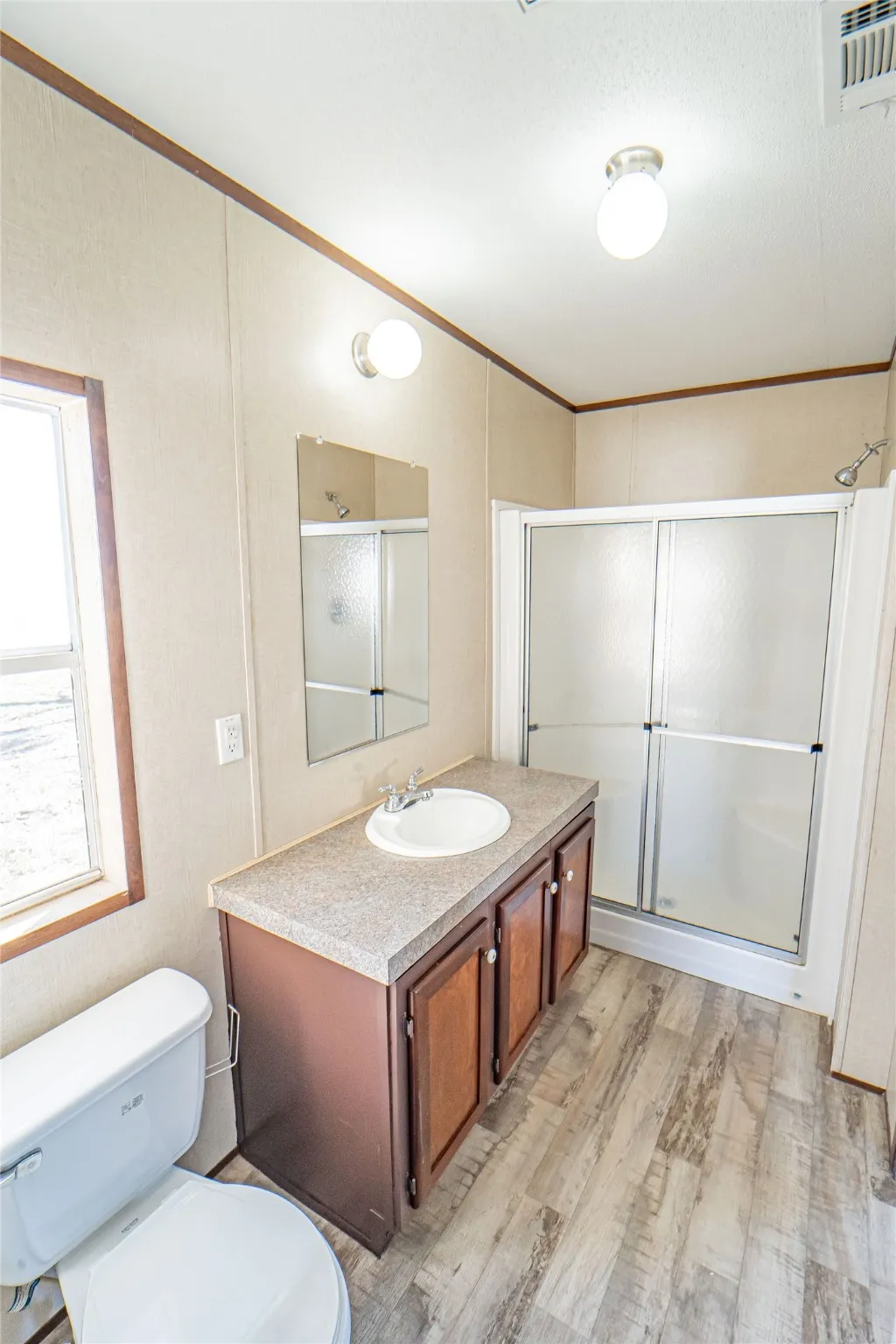 Bathroom with ornamental molding, vanity, light wood finished floors, and a stall shower