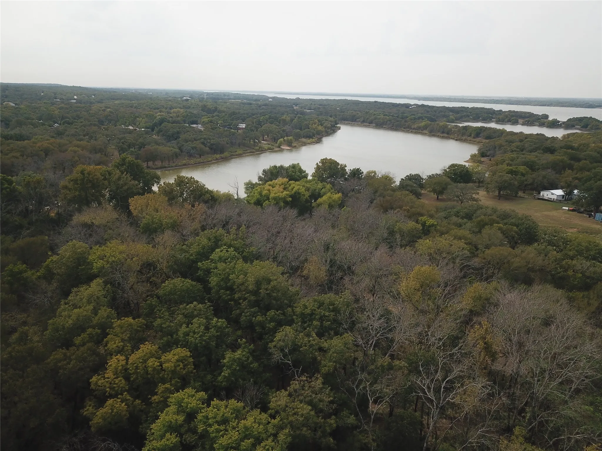 Aerial view of property and surrounding area with a forest and a nearby body of water