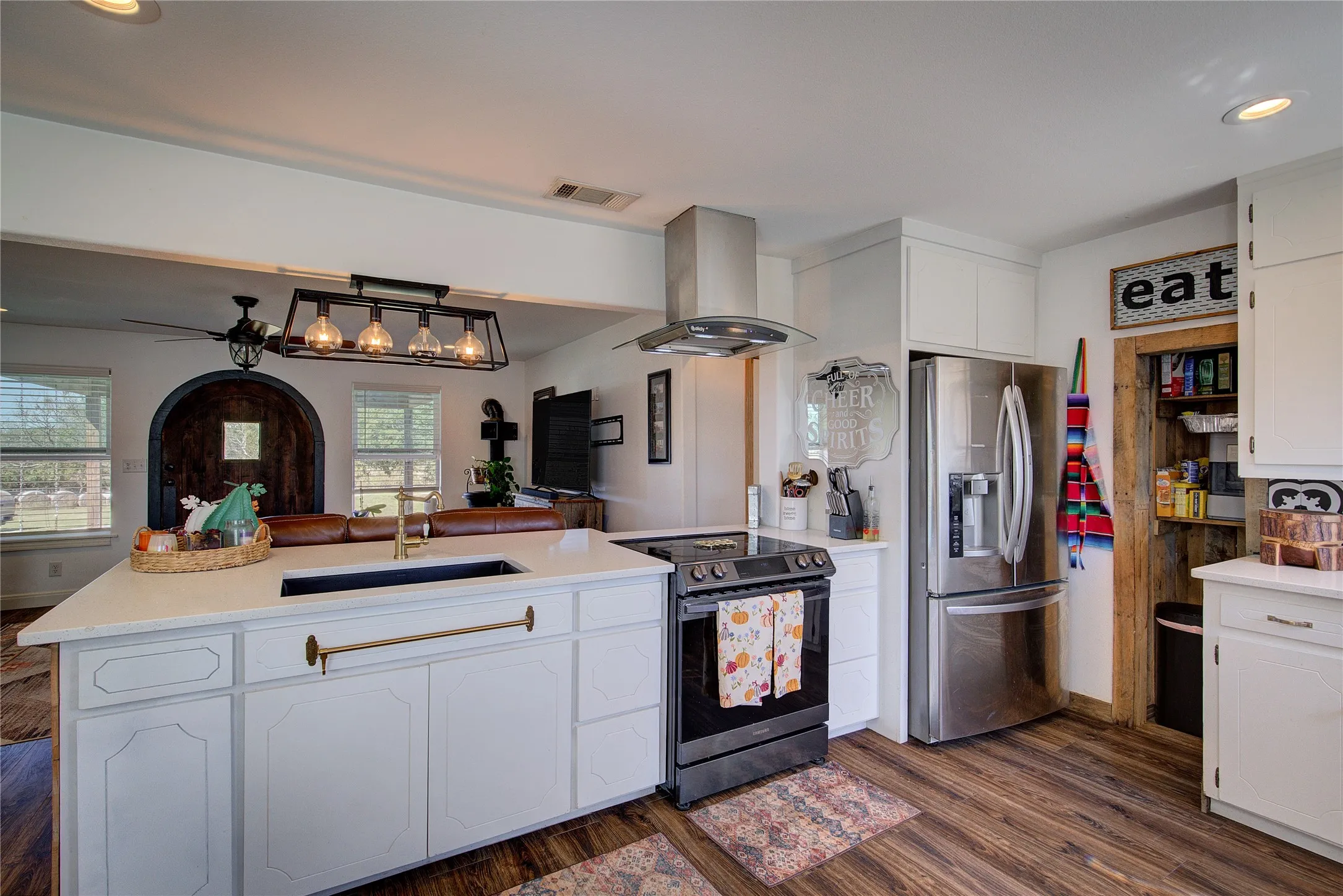 Kitchen has pantry nook, pendant lights over the breakfast bar, farm-style undermount sink.