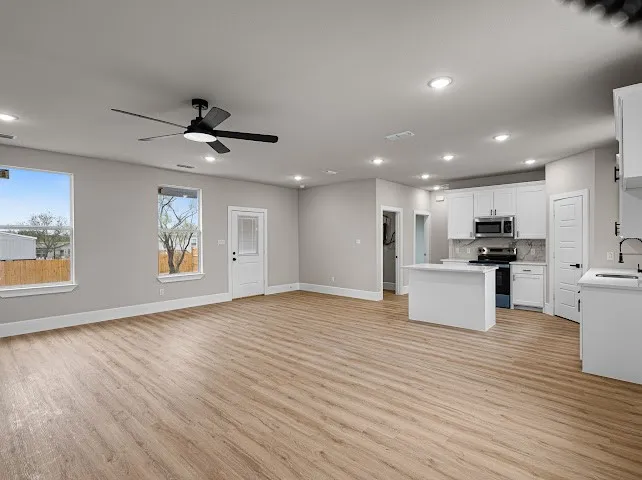 Kitchen with a kitchen island, white cabinets, open floor plan, light wood-style floors, and stainless steel appliances