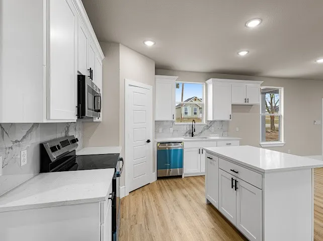 Kitchen featuring appliances with stainless steel finishes, white cabinets, light wood-type flooring, decorative backsplash, and recessed lighting