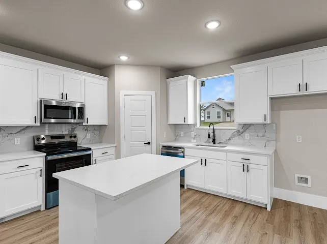 Kitchen featuring appliances with stainless steel finishes, white cabinets, light wood finished floors, a kitchen island, and tasteful backsplash