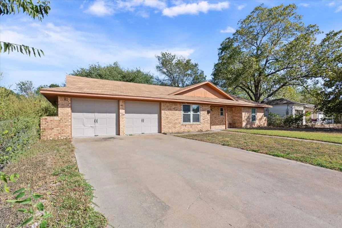 Single story home featuring concrete driveway, brick siding, an attached garage, a front lawn, and roof with shingles