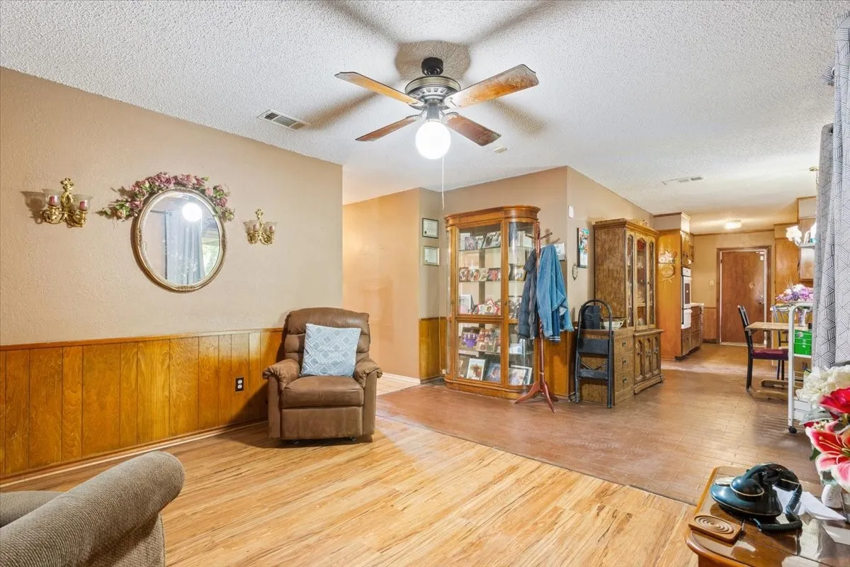 Living area featuring light wood-style floors, a textured ceiling, wood walls, wainscoting, and ceiling fan