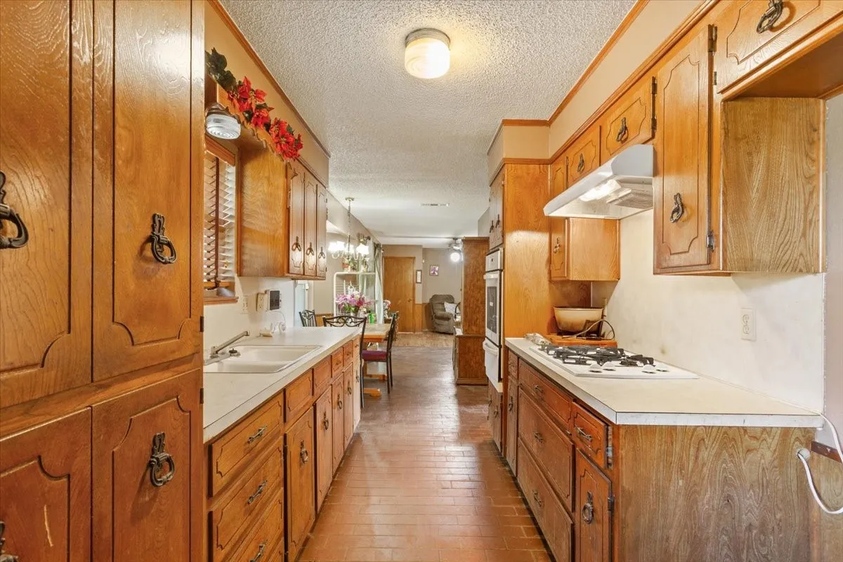 Kitchen with light countertops, a textured ceiling, brown cabinetry, under cabinet range hood, and white gas cooktop