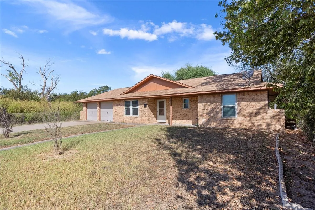 Ranch-style home featuring brick siding, concrete driveway, a front lawn, an attached garage, and roof with shingles